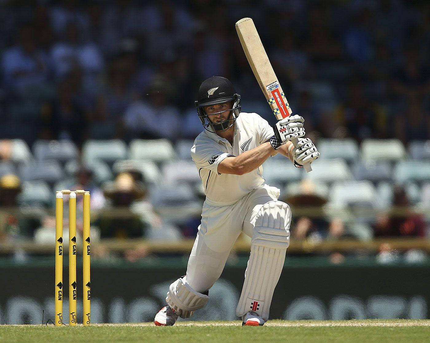 kane williamson 桌布 壁紙 — 一名身穿白色球衣的板球擊球手在陽光明媚的綠色球場上，強力揮動球棒擊向靠近黃色三柱門的球。