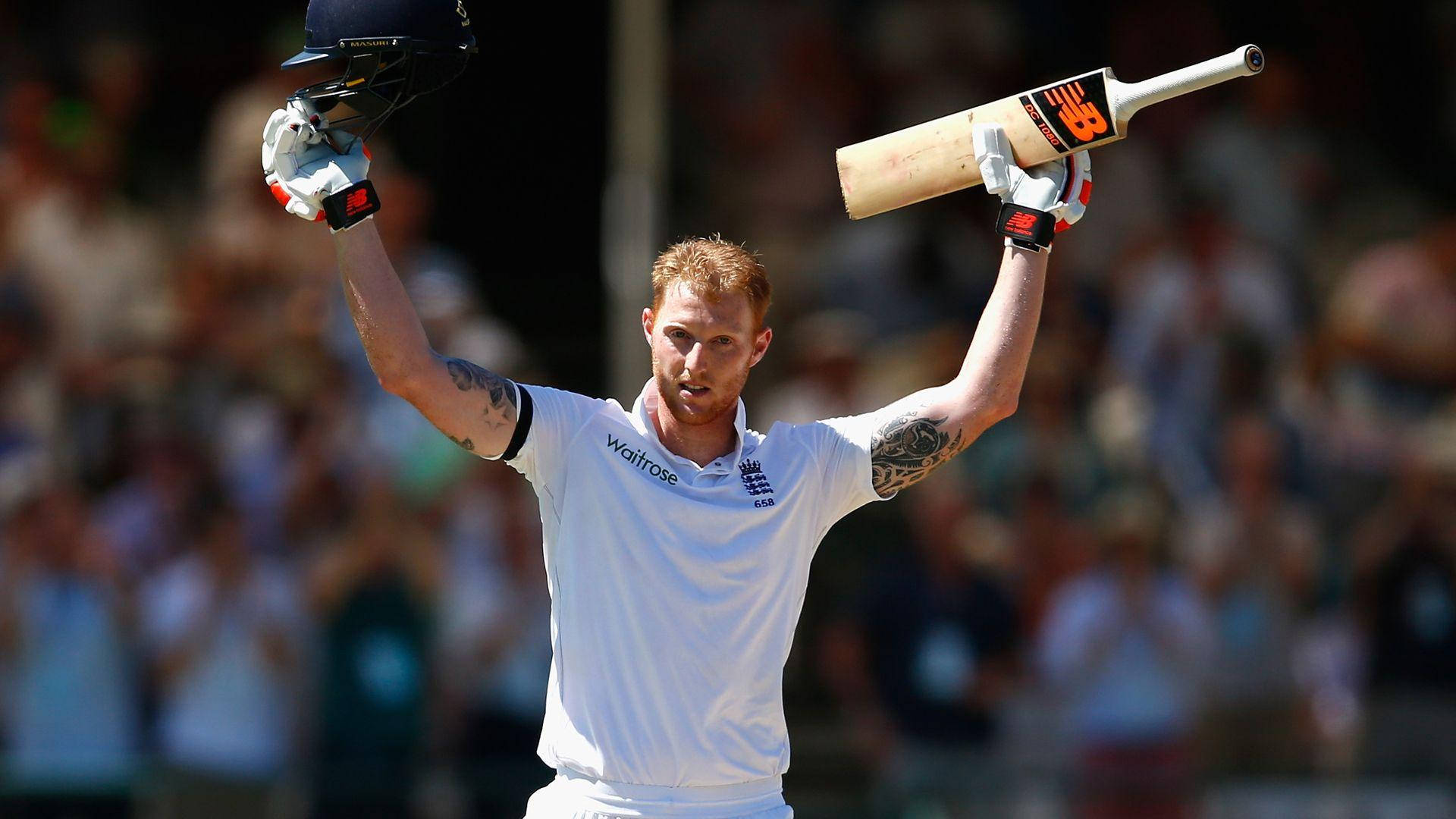 Ben Stokes 桌布 壁紙 — 一名身穿白色球衣的板球運動員在陽光明媚的球場上，勝利地將球棒和頭盔高舉過頭頂。