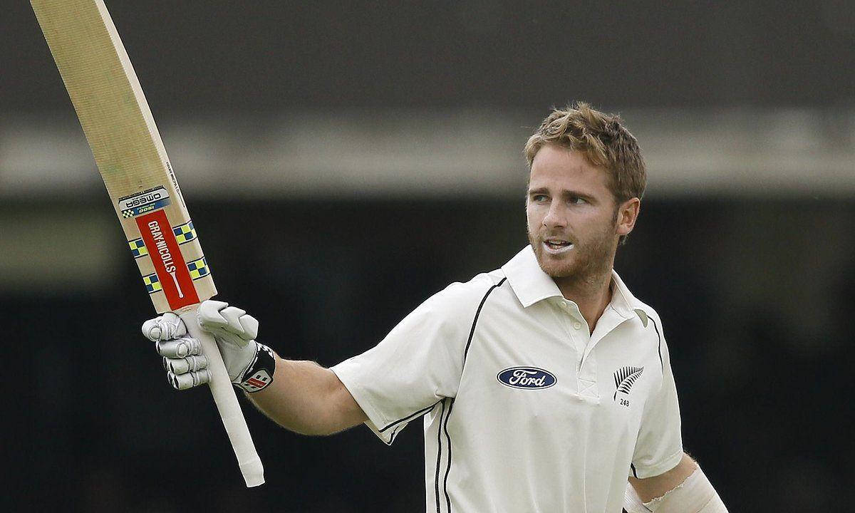 kane williamson 桌布 壁紙 — 一名身穿白色球衣的板球選手高舉球棒，臉上帶著勝利的表情，背景是模糊的體育場。
