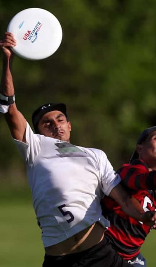 Athlete 桌布 壁紙 — 一名身穿白色球衣的男性極限飛盤選手跳起接住USA Ultimate飛盤，而身穿紅黑色球衣的對手則在防守。