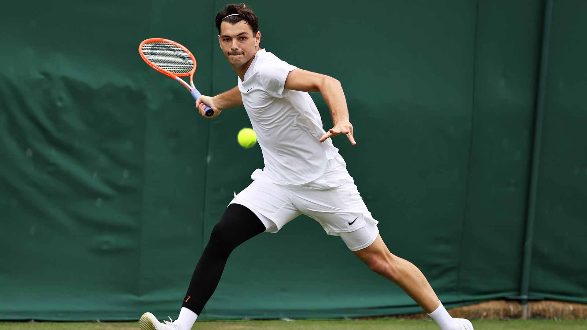 Tennis 桌布 壁紙 — 一名身穿白色球衣的男網球選手在草地場上向前撲出，用橙色球拍擊打一個亮黃色的球。