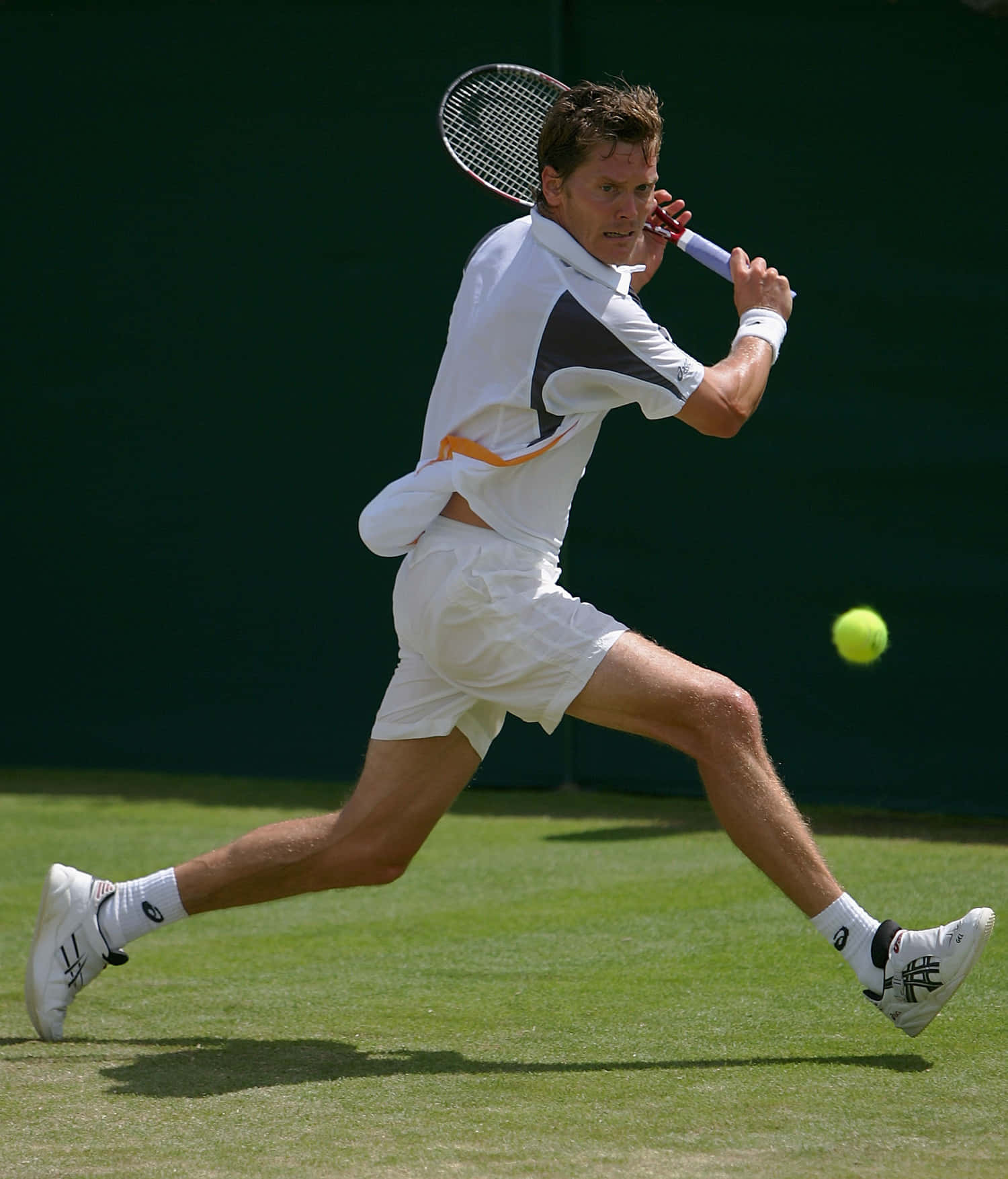 Tennis 桌布 壁紙 — 一名身穿白色球衣的男網球選手在草地場上向前猛撲，以高度專注擊打黃色網球。