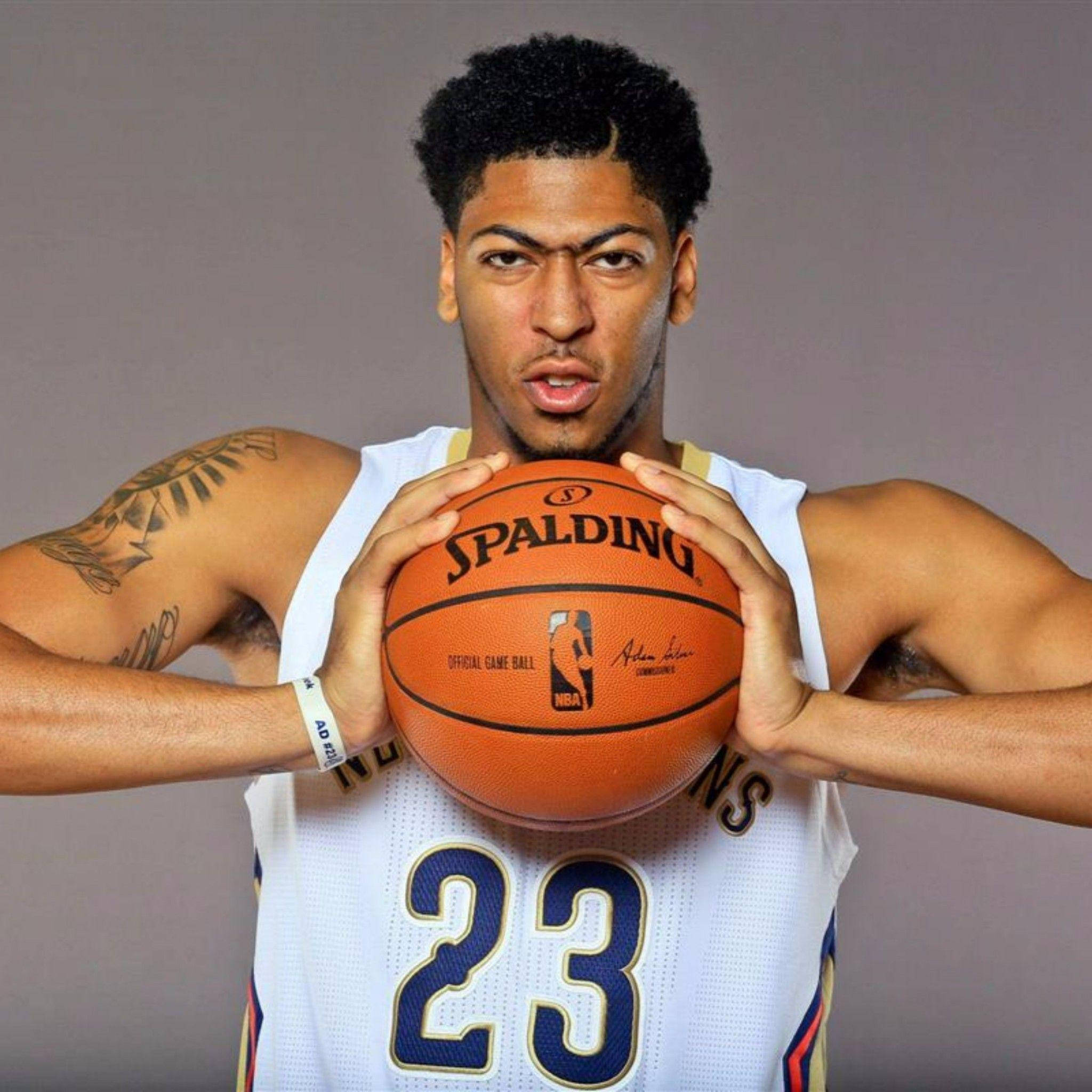 Anthony Davis 桌布 壁紙 — 一名身穿白色球衣的籃球運動員，在純灰色背景下，專注地拿著一個橙色的 Spalding NBA 比賽用球。