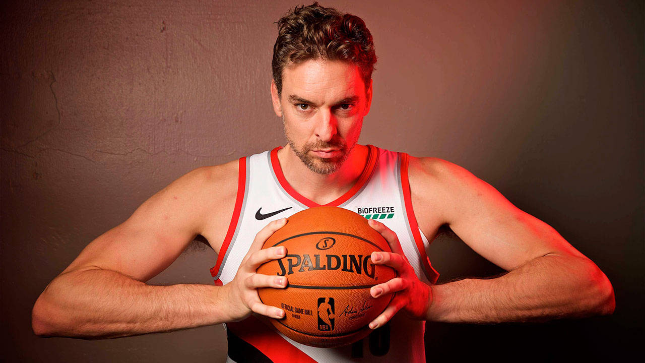 Pau Gasol 桌布 壁紙 — 一名身穿白色球衣的籃球運動員，在戲劇性的紅色燈光下，對著有紋理的牆壁緊握著 Spalding 球。