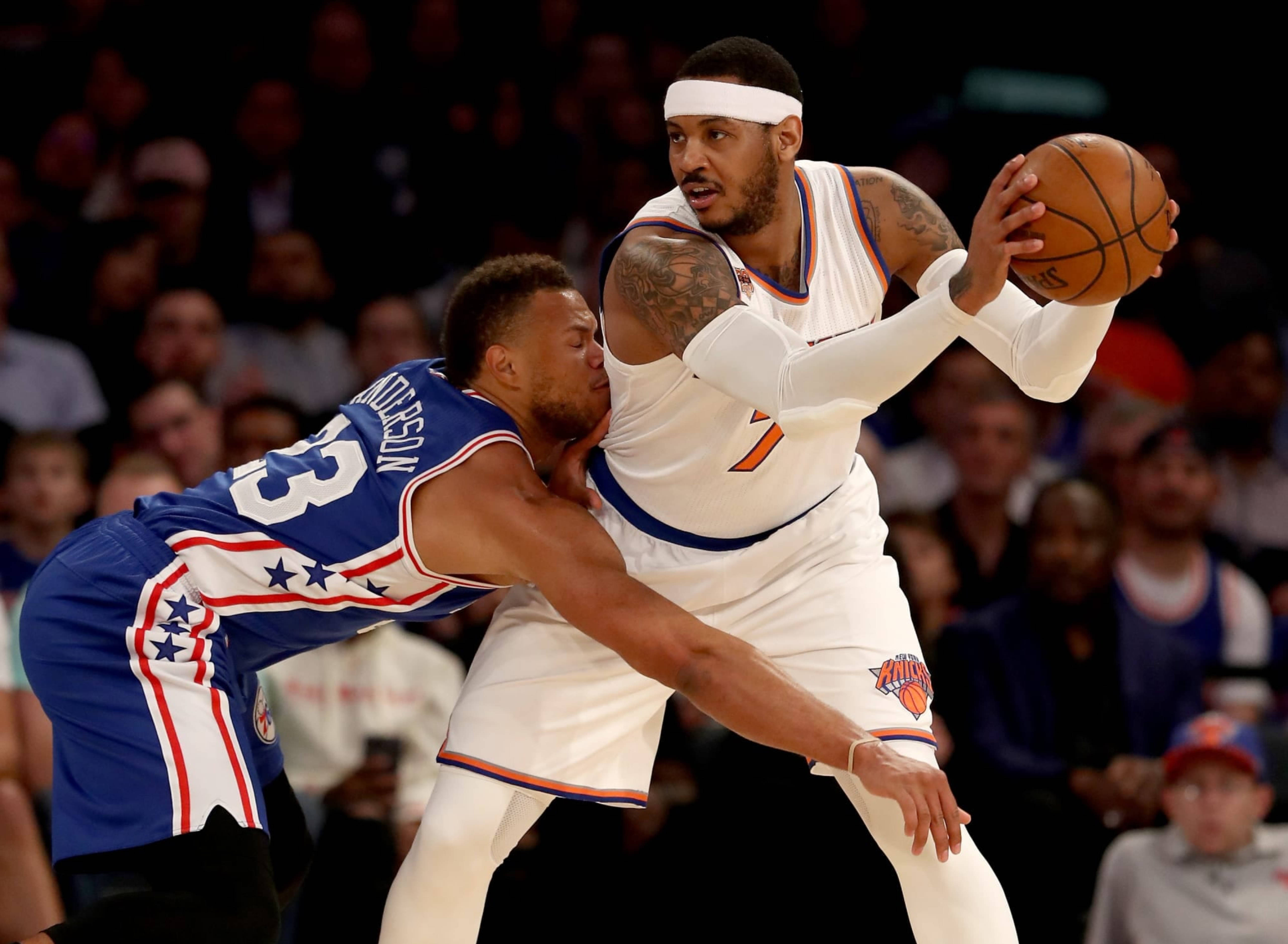 Carmelo 桌布 壁紙 — 一名身穿白色球衣的籃球運動員在場館燈光下進行激烈比賽時，越過一名身穿藍色球衣的防守球員。