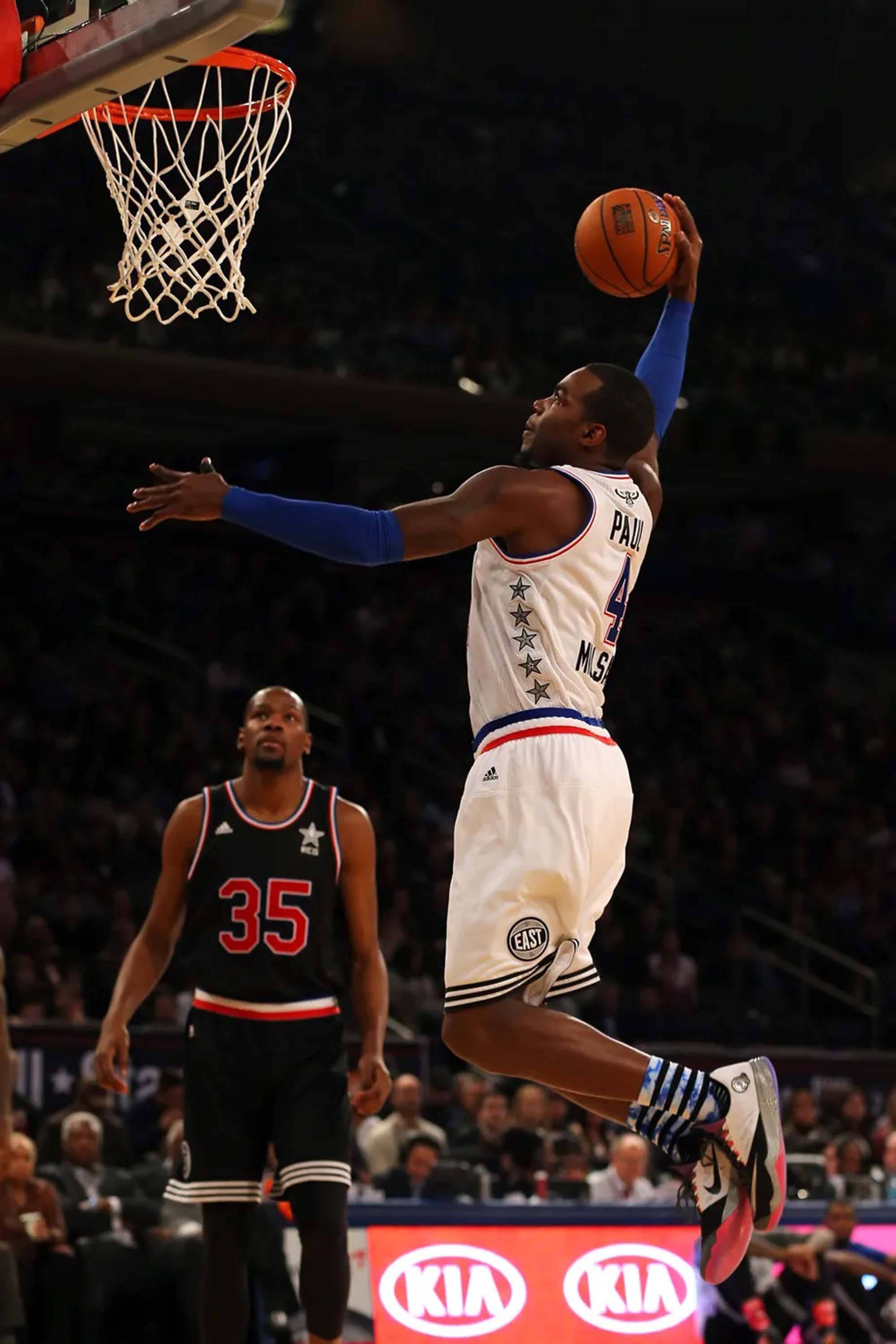 paul millsap 桌布 壁紙 — 一名身穿白色球衣的籃球運動員在場館燈光下灌籃，另一名球員從下方觀看。