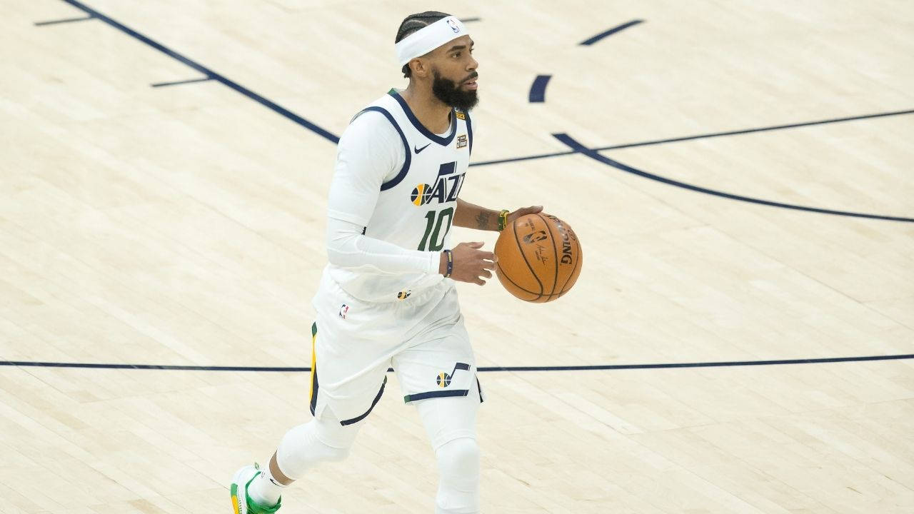 mike conley 桌布 壁紙 — 一名身穿白色球衣的籃球運動員在明亮的場館燈光下，於拋光木地板上運球。