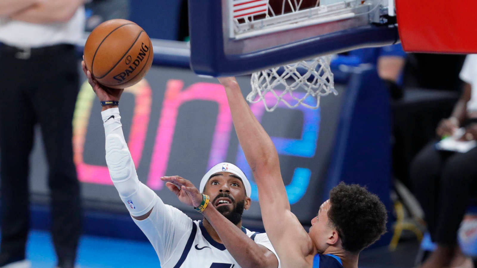mike conley 桌布 壁紙 — 一名身穿白色球衣的籃球運動員在明亮的場館燈光下跳起灌籃，而防守球員試圖封阻。