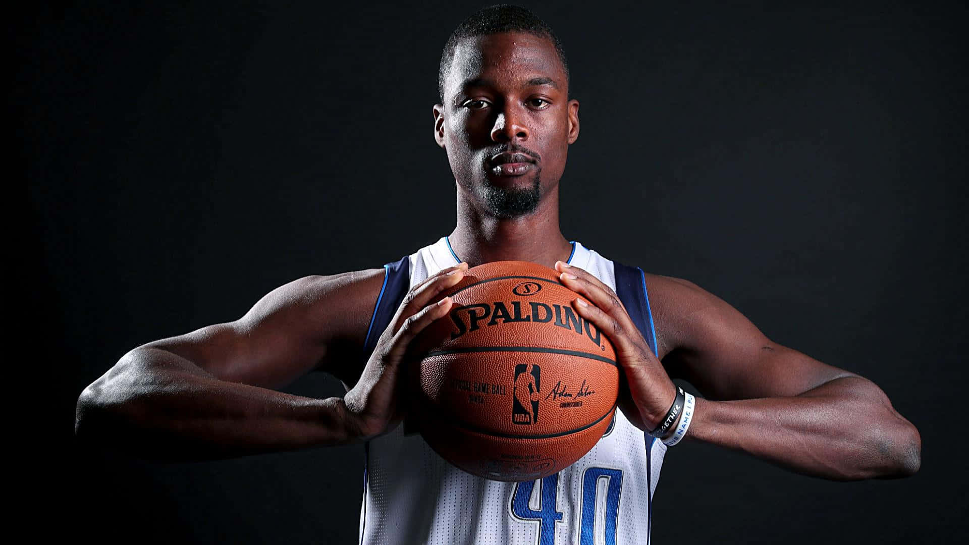 NBA 桌布 壁紙 — 一名身穿白色球衣的籃球運動員在深色攝影棚背景下手持Spalding籃球。