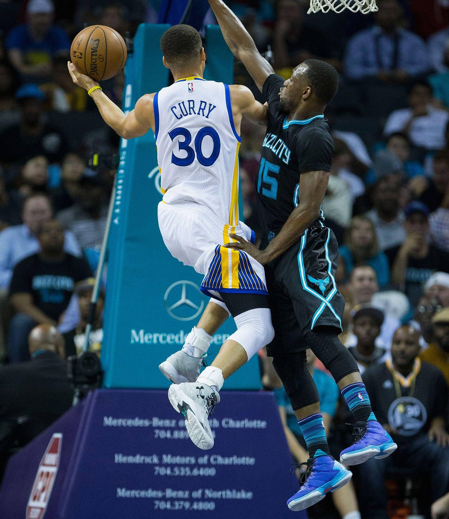Kemba Walker 桌布 壁紙 — 一名身穿白色球衣的籃球運動員在激烈的比賽中跳向籃框，同時被一名身穿黑色球衣的對手防守。