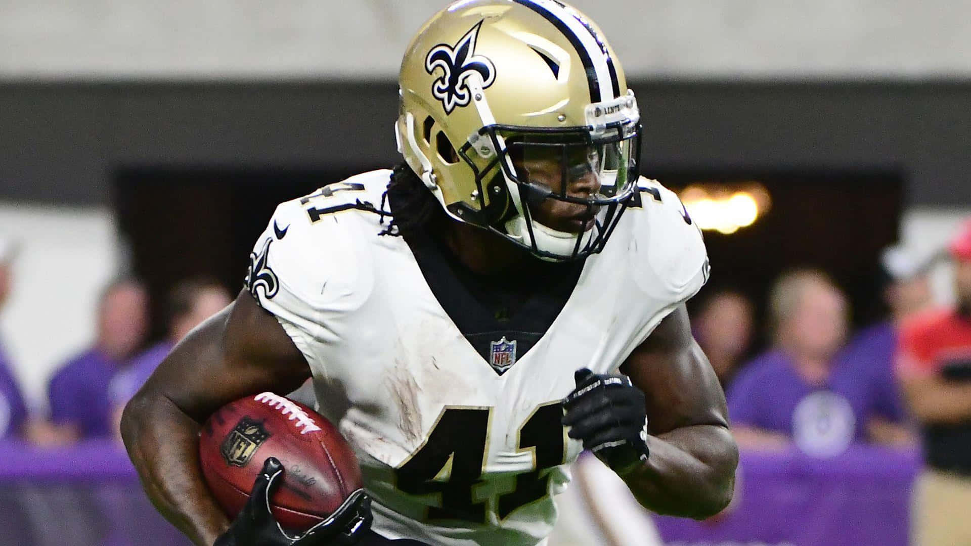 Alvin Kamara 桌布 壁紙 — 一名身穿白色球衣的紐奧良聖徒美式足球員在球場燈光下比賽中持球衝刺。