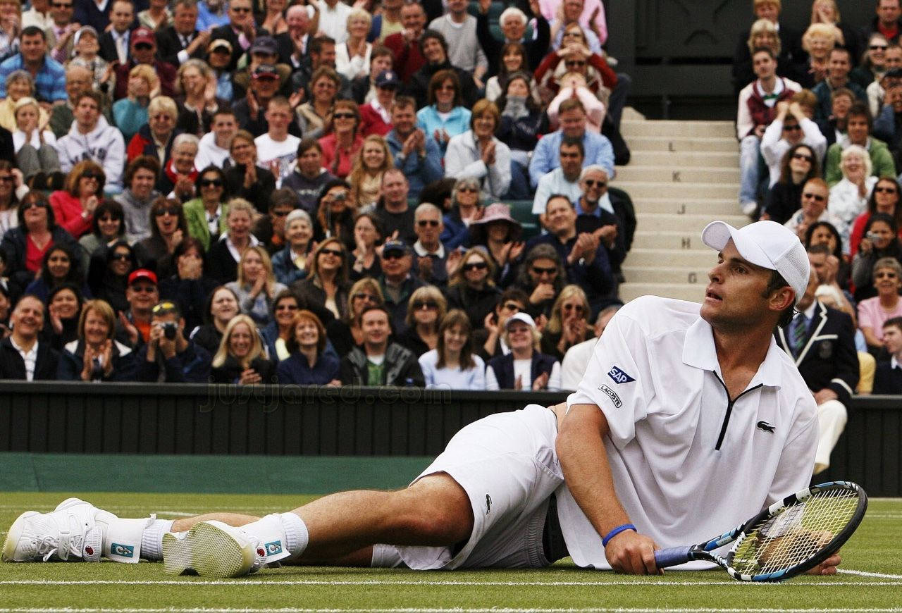 Tennis 桌布 壁紙 — 一名身穿白色球衣的網球選手筋疲力盡地躺在草地場上，身後觀眾歡呼。