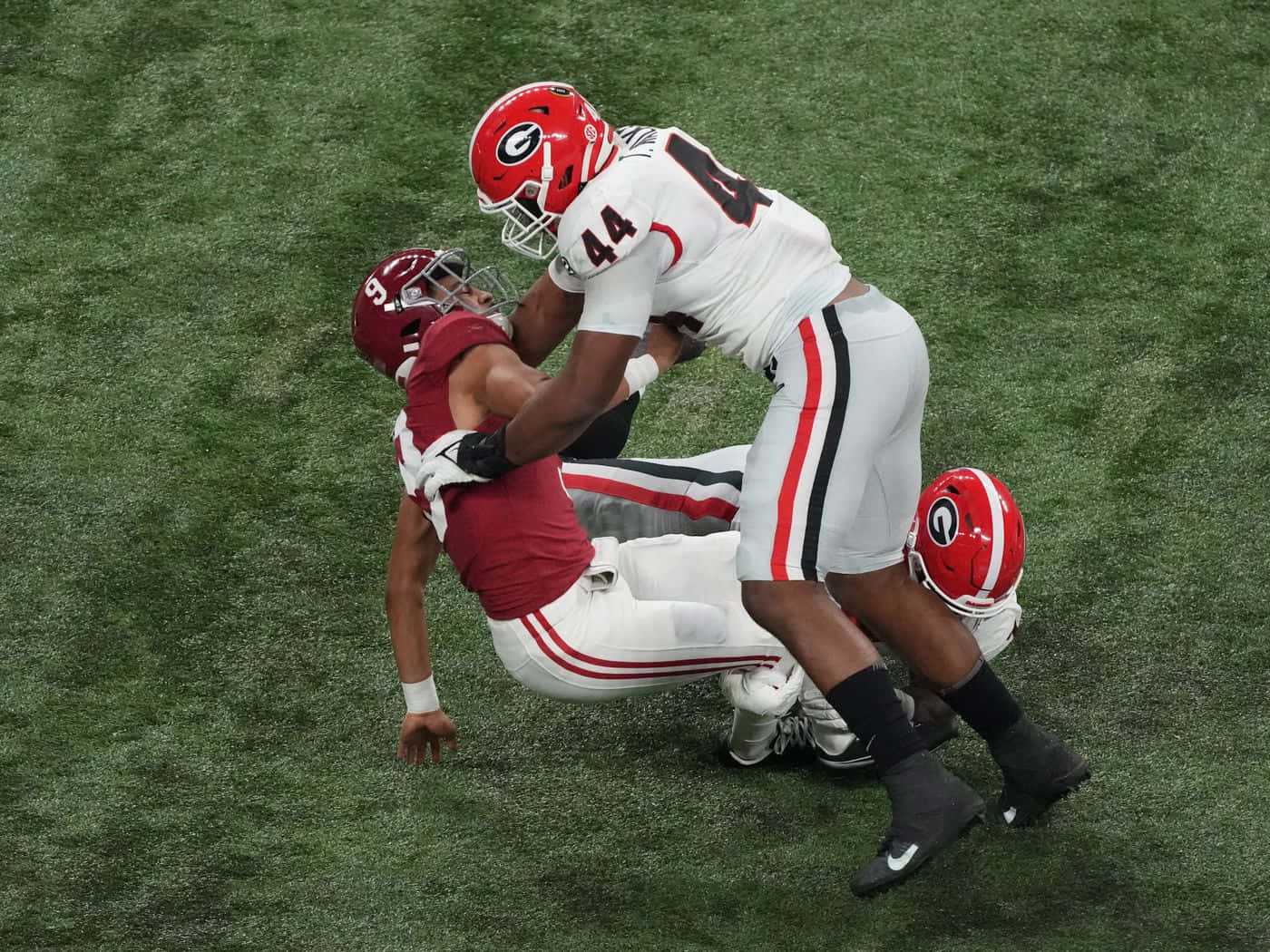 Alabama Football 桌布 壁紙 — 一名身穿白色球衣的足球員在充滿活力的綠色草地上攔截一名身穿紅色球衣的對手。