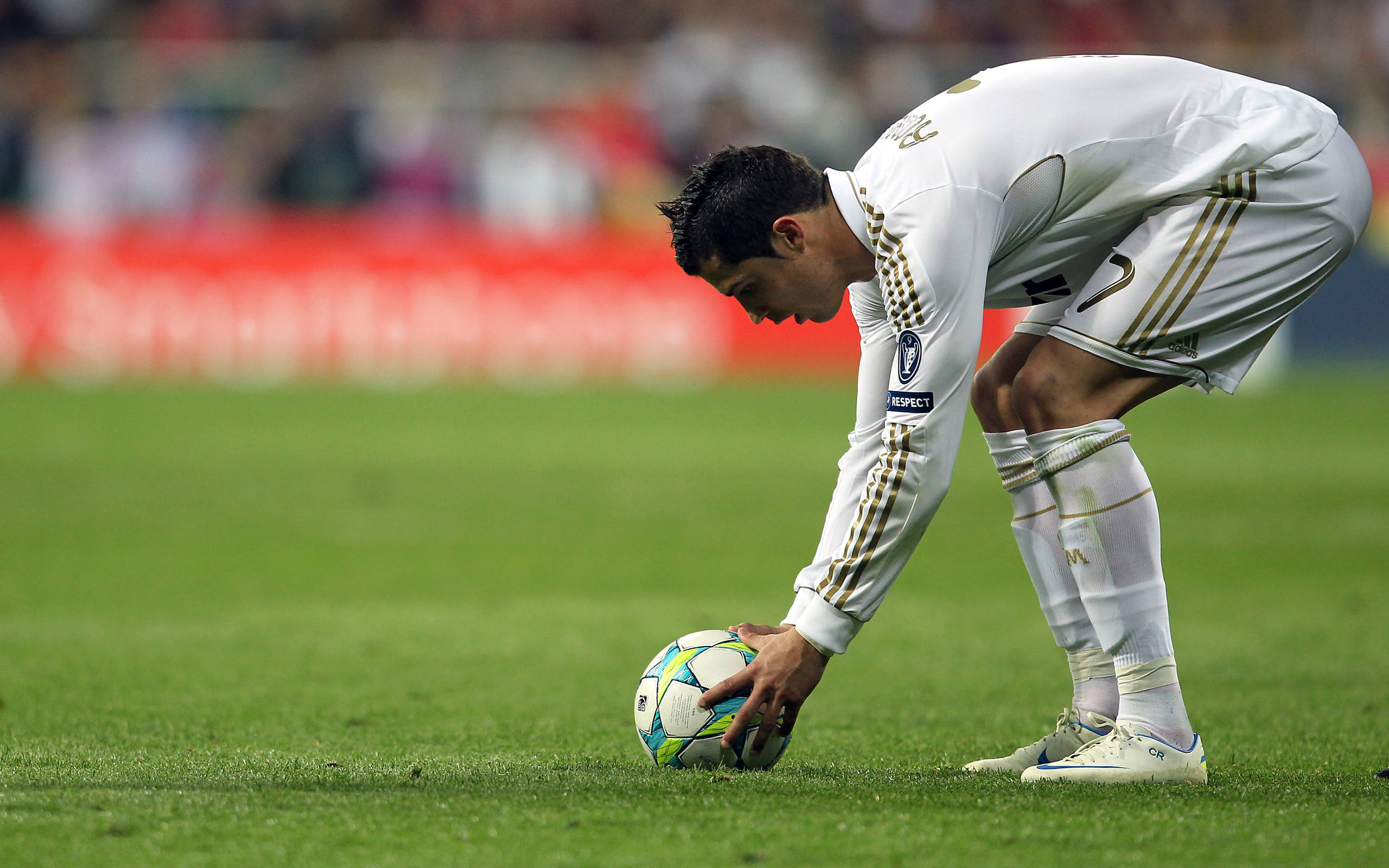 Cr7 桌布 壁紙 — 一名身穿白色球衣的足球員在體育場燈光下，在充滿活力的綠色球場上彎腰觸碰一個色彩繽紛的足球。