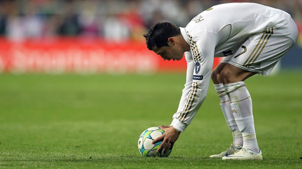 Ronaldo 桌布 壁紙 — 一名身穿白色球衣的足球員彎腰觸摸色彩繽紛的足球，在充滿活力的綠色草地上，在明亮的日光下。