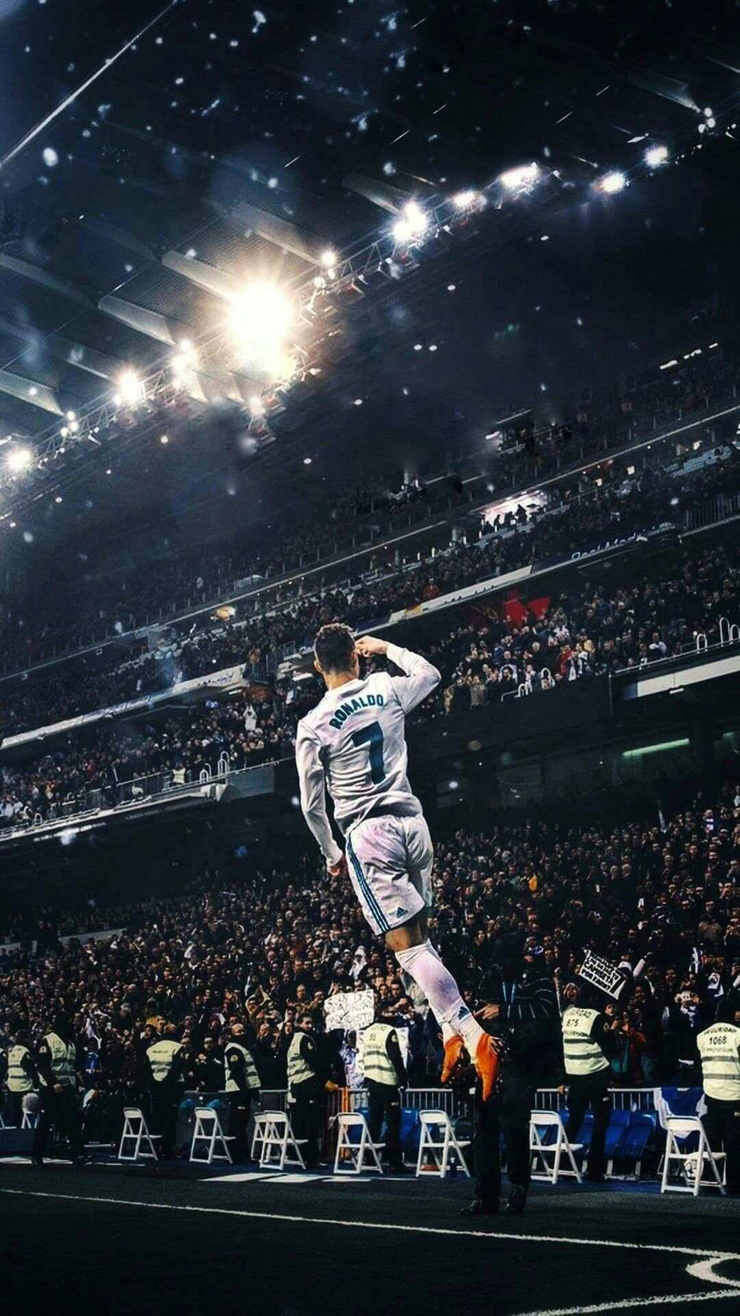 Ronaldo 桌布 壁紙 — 一名身穿白色球衣的足球運動員在擠滿觀眾的體育館內，在明亮的泛光燈下，紙屑飄落時勝利地跳躍。
