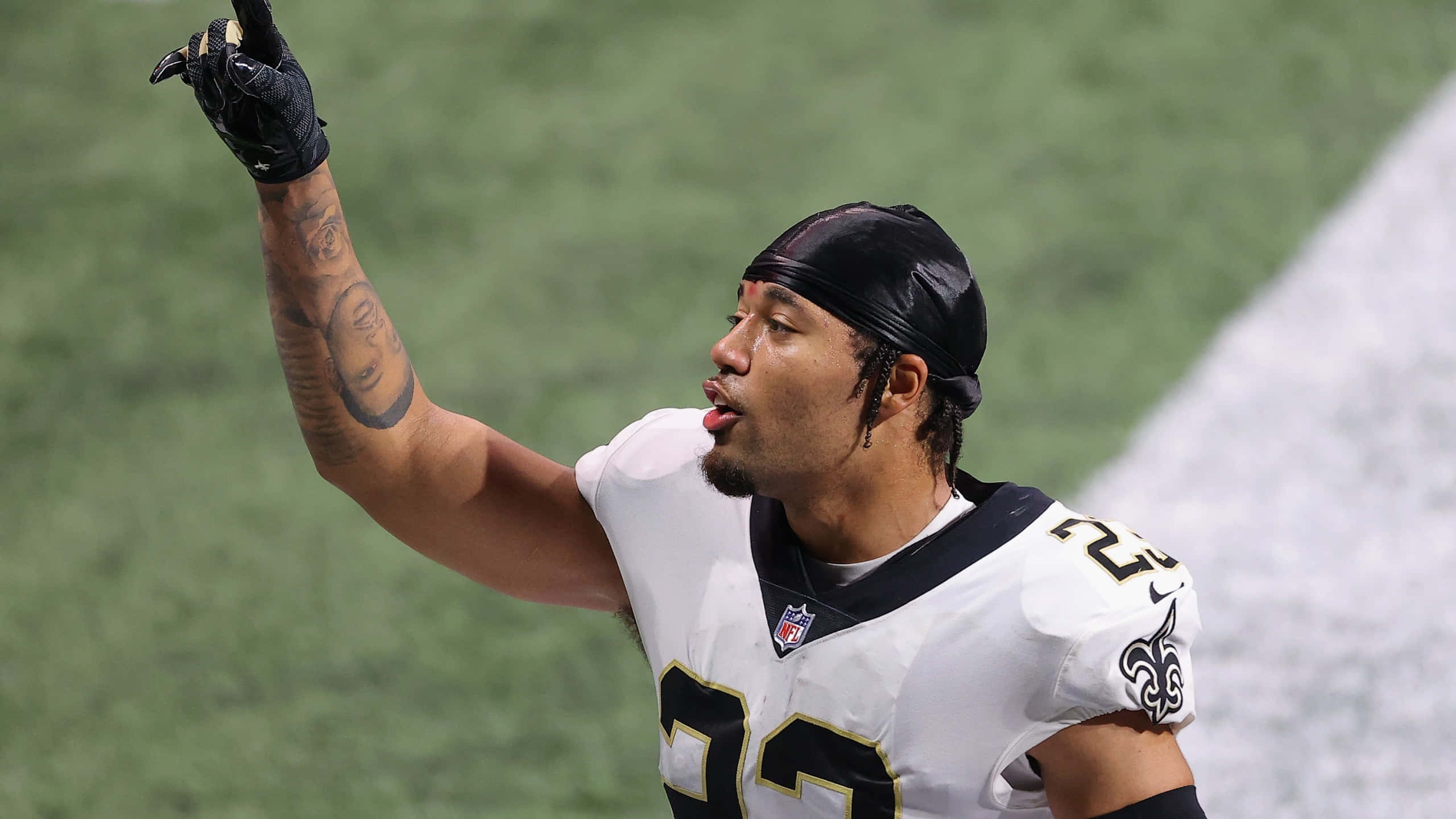 New Orleans Saints 桌布 壁紙 — 一名身穿白色球衣的足球運動員在綠色球場上高舉右手、伸出舌頭慶祝。