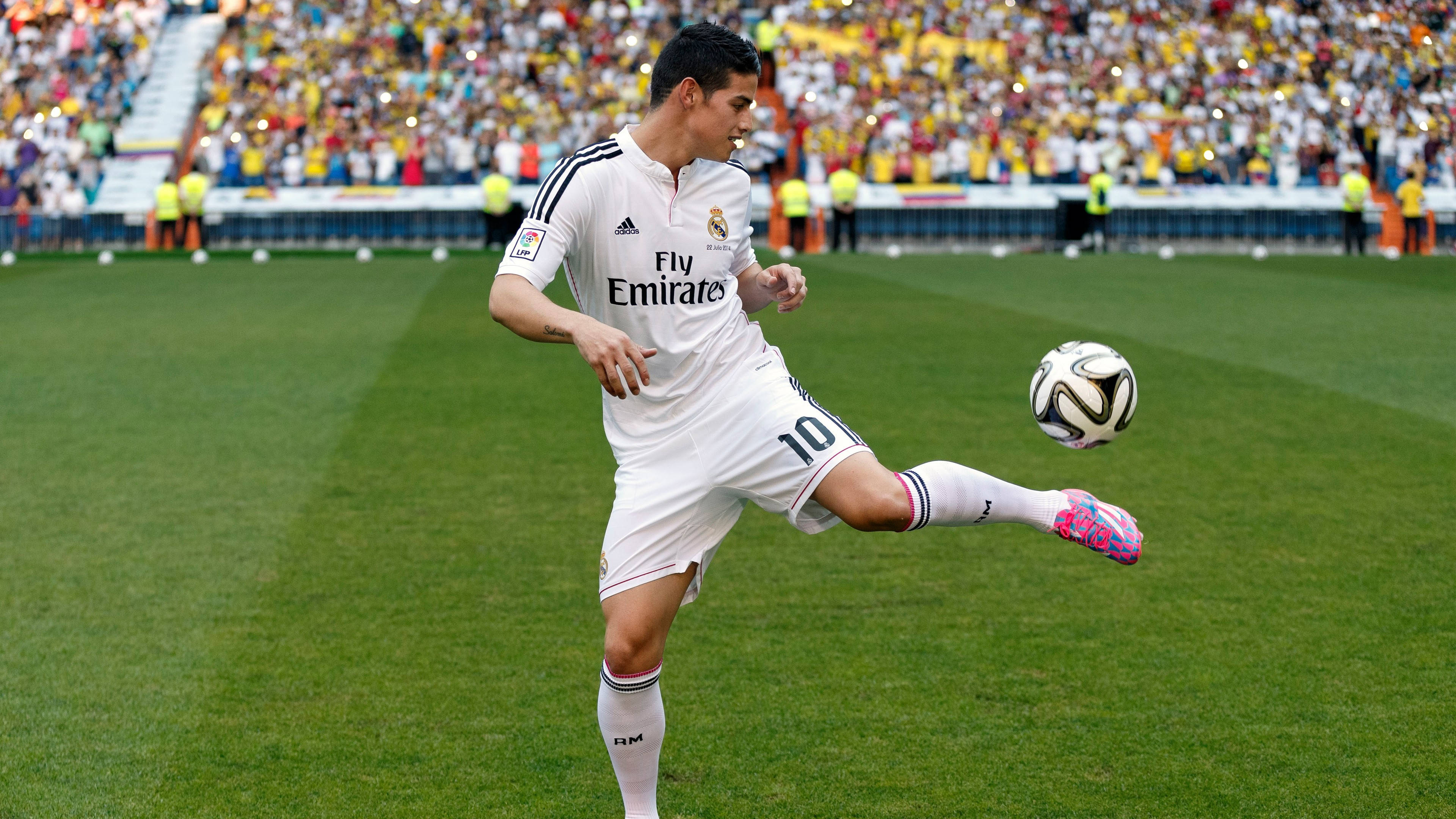 James Rodriguez 桌布 壁紙 — 一名身穿白色皇家馬德里球衣的足球運動員在充滿活力的綠色球場上凌空踢球，背景是座無虛席的體育場。