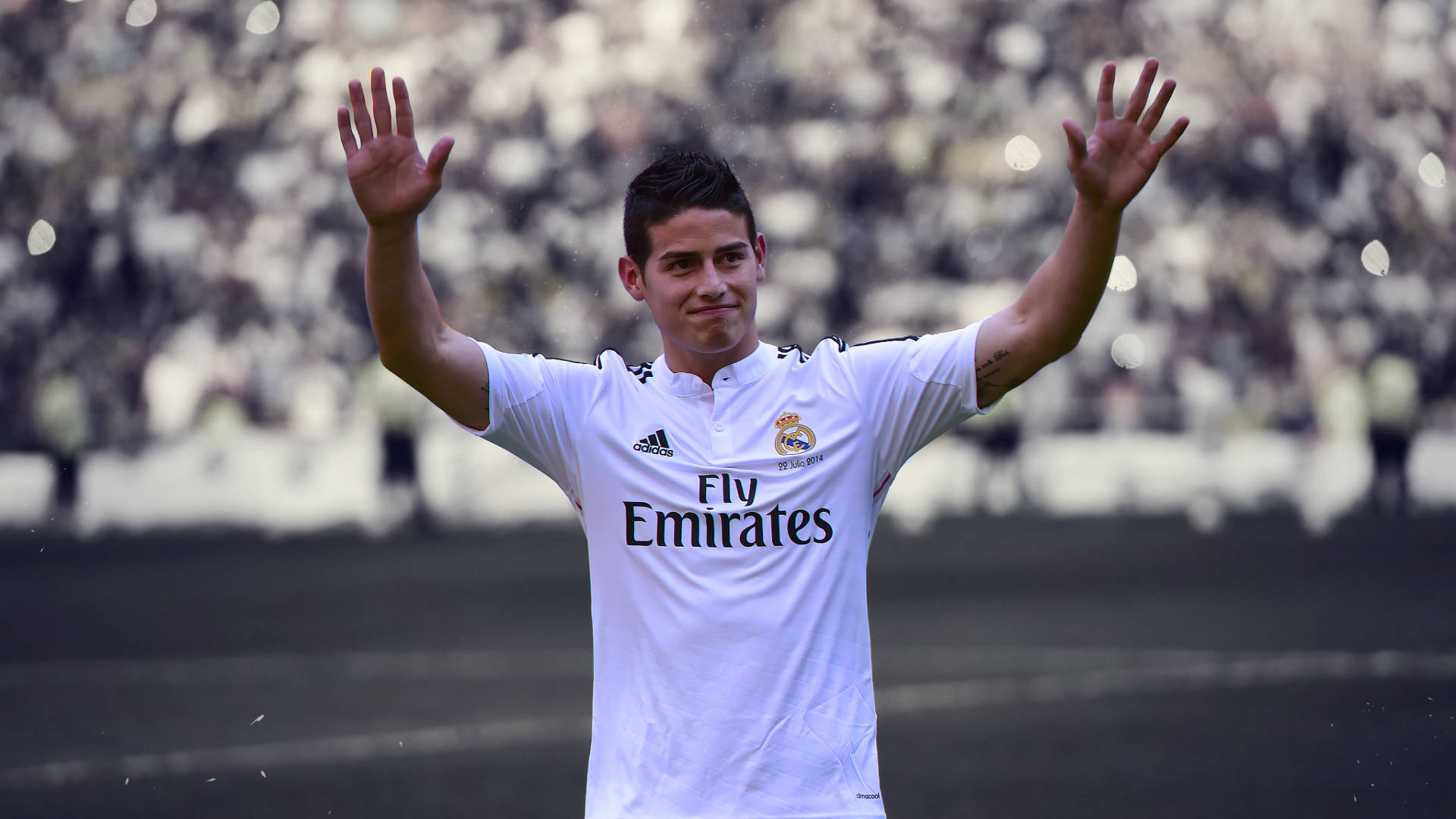 James Rodriguez 桌布 壁紙 — 一名身穿白色皇家馬德里球衣的足球運動員在球場上向球迷揮手，身後是模糊的觀眾。