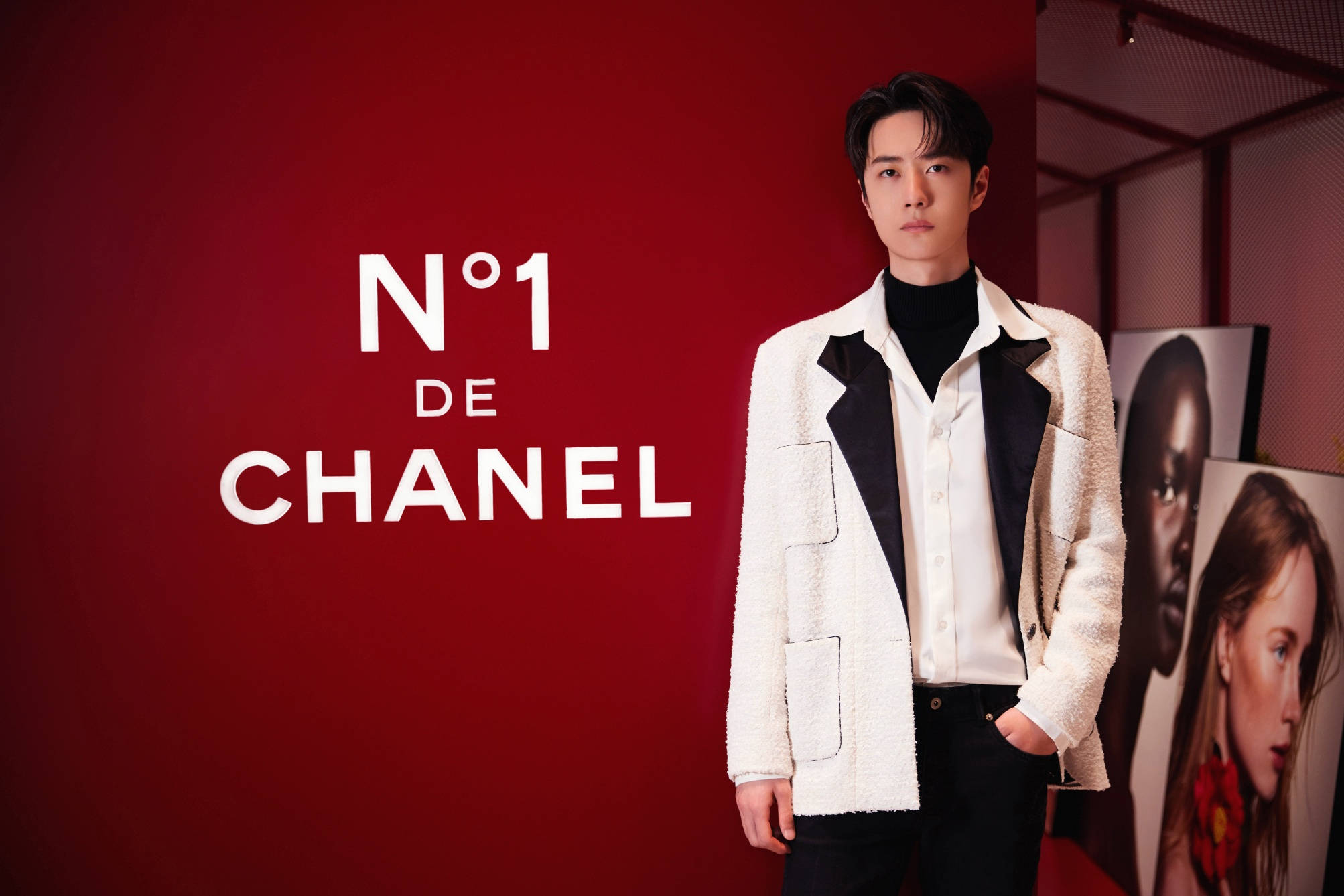 Wang Yibo 桌布 壁紙 — 一名身穿白色紋理 Chanel 外套的男子自信地站在一面印有 'N°1 DE CHANEL' 字樣的搶眼紅牆前。