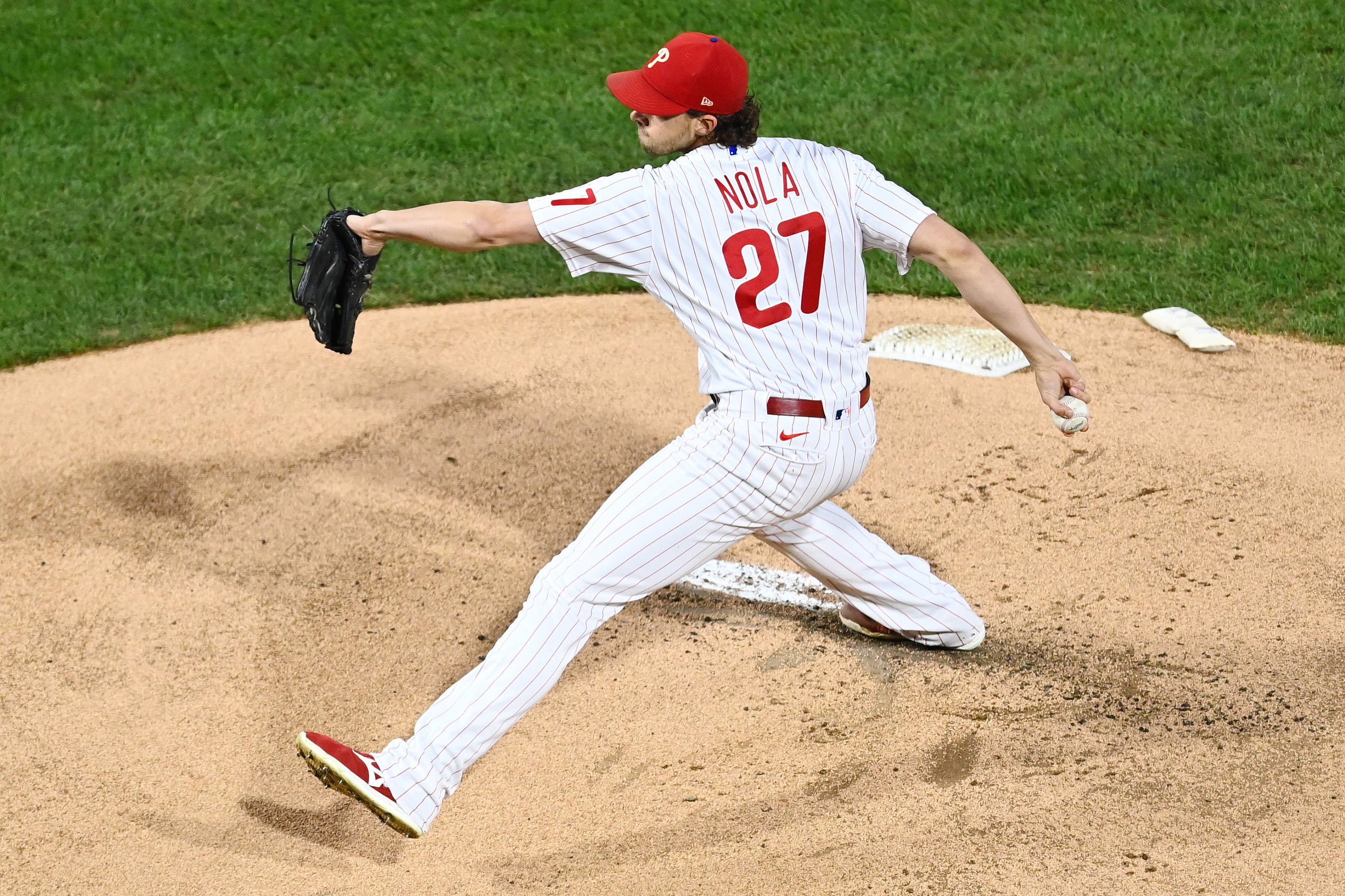 Phillies 桌布 壁紙 — 一名身穿白色細條紋制服、紅色27號球衣和帽子的棒球投手，正在綠色場地的投手丘上投球。
