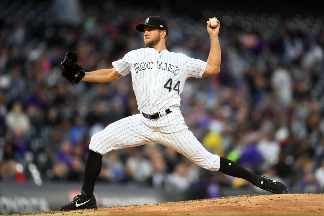 Colorado Rockies 桌布 壁紙 — 一名身穿白色細條紋洛磯隊球衣的棒球投手，在夜間比賽的球場燈光下準備投球。