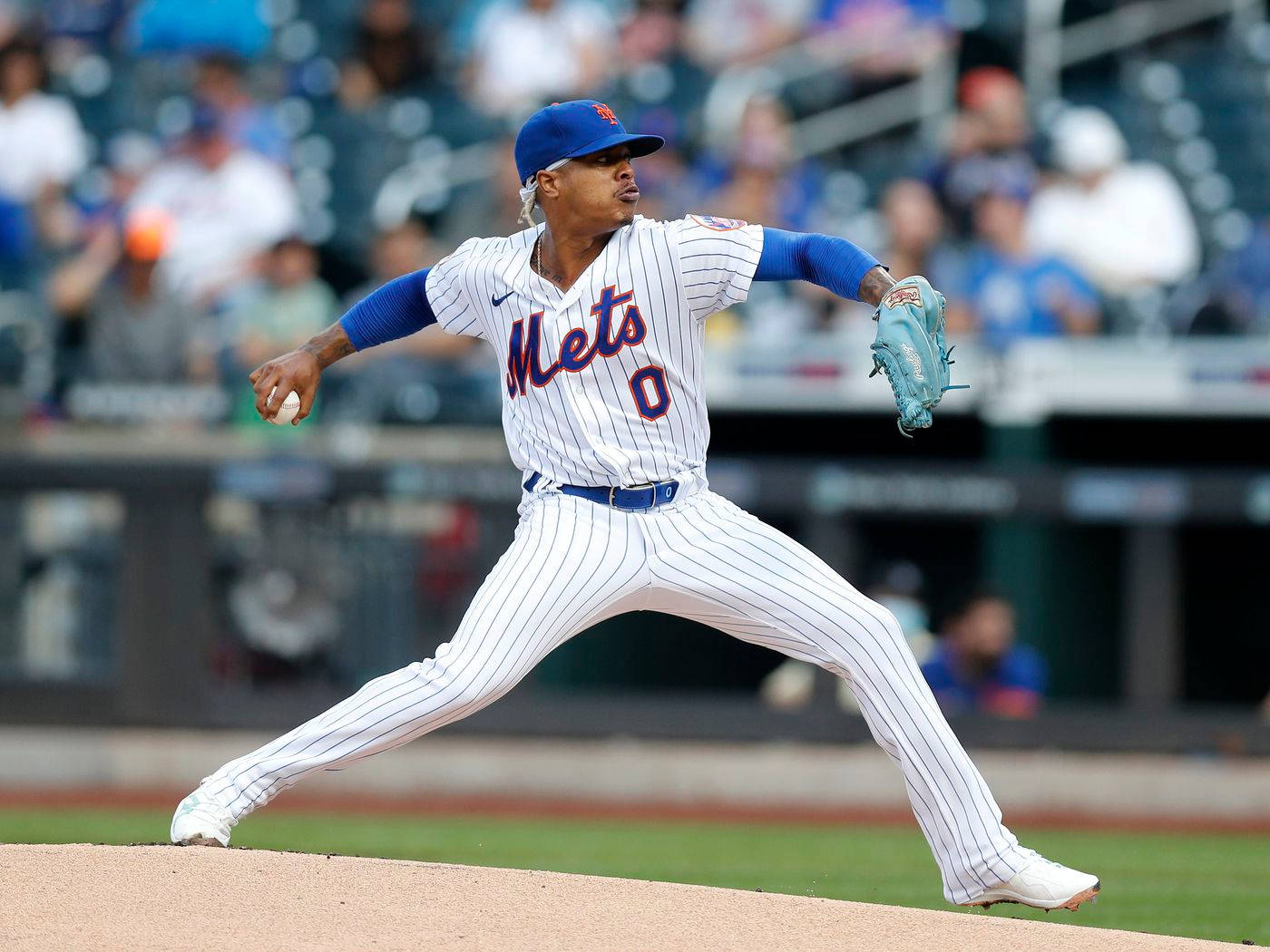 Marcus Stroman 桌布 壁紙 — 一名身穿白色細條紋球衣的Mets棒球投手，在陽光明媚的投手丘上投球，背景是模糊的球場觀眾。