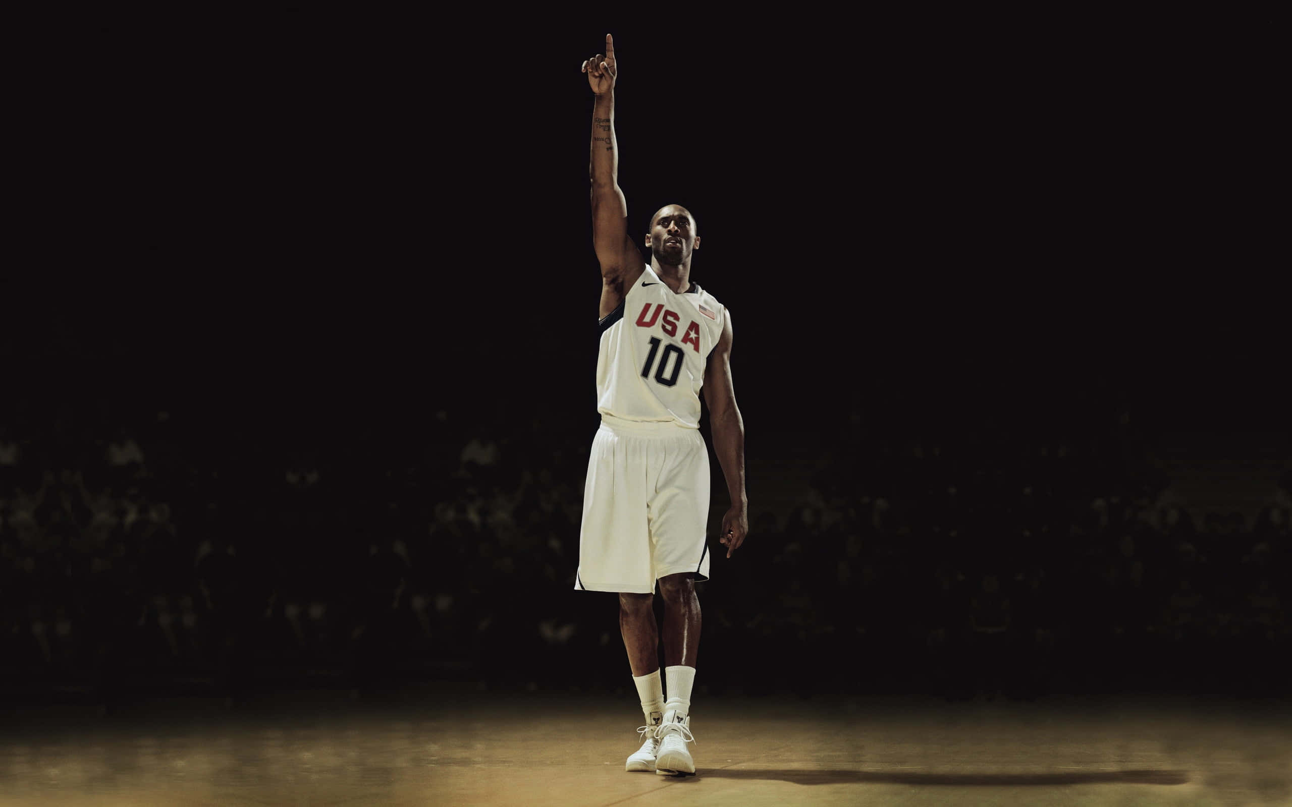 NBA 桌布 壁紙 — 一名身穿白色美國隊10號球衣的籃球運動員獨自站在燈光昏暗的球場上，單手指向上方。