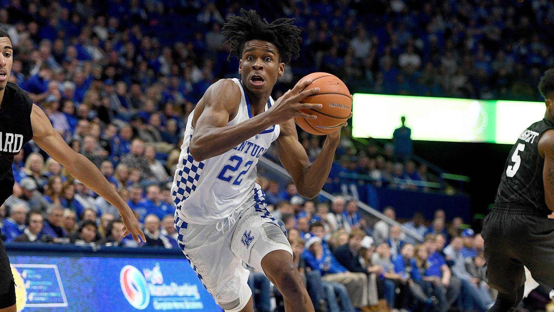 Shai Gilgeous Alexander 桌布 壁紙 — 一名身穿白色肯塔基球衣的籃球運動員在擠滿觀眾的場館中運球，同時受到對手的防守。