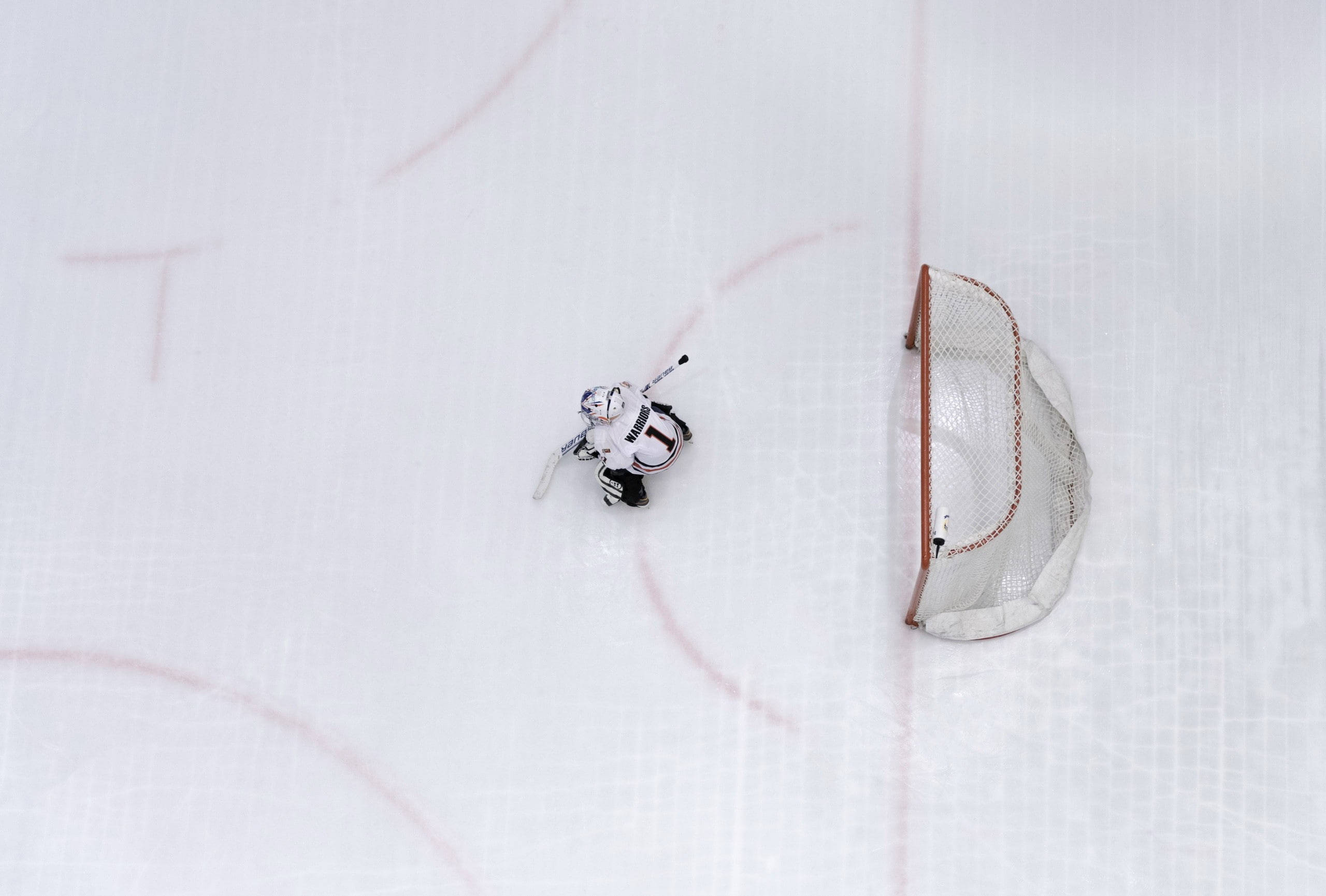 hockey 桌布 壁紙 — 一名身穿白色裝備的冰球守門員在標有紅線的清晰冰場上蹲在球門附近。