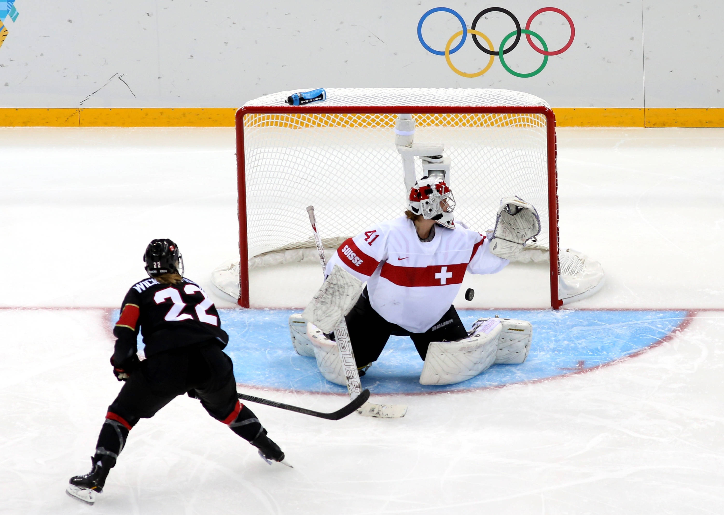 Winter Olympics 桌布 壁紙 — 一名身穿白色裝備的瑞士冰球守門員飛身撲救，阻擋射門，而一名身穿黑色的對方球員正溜向球門。