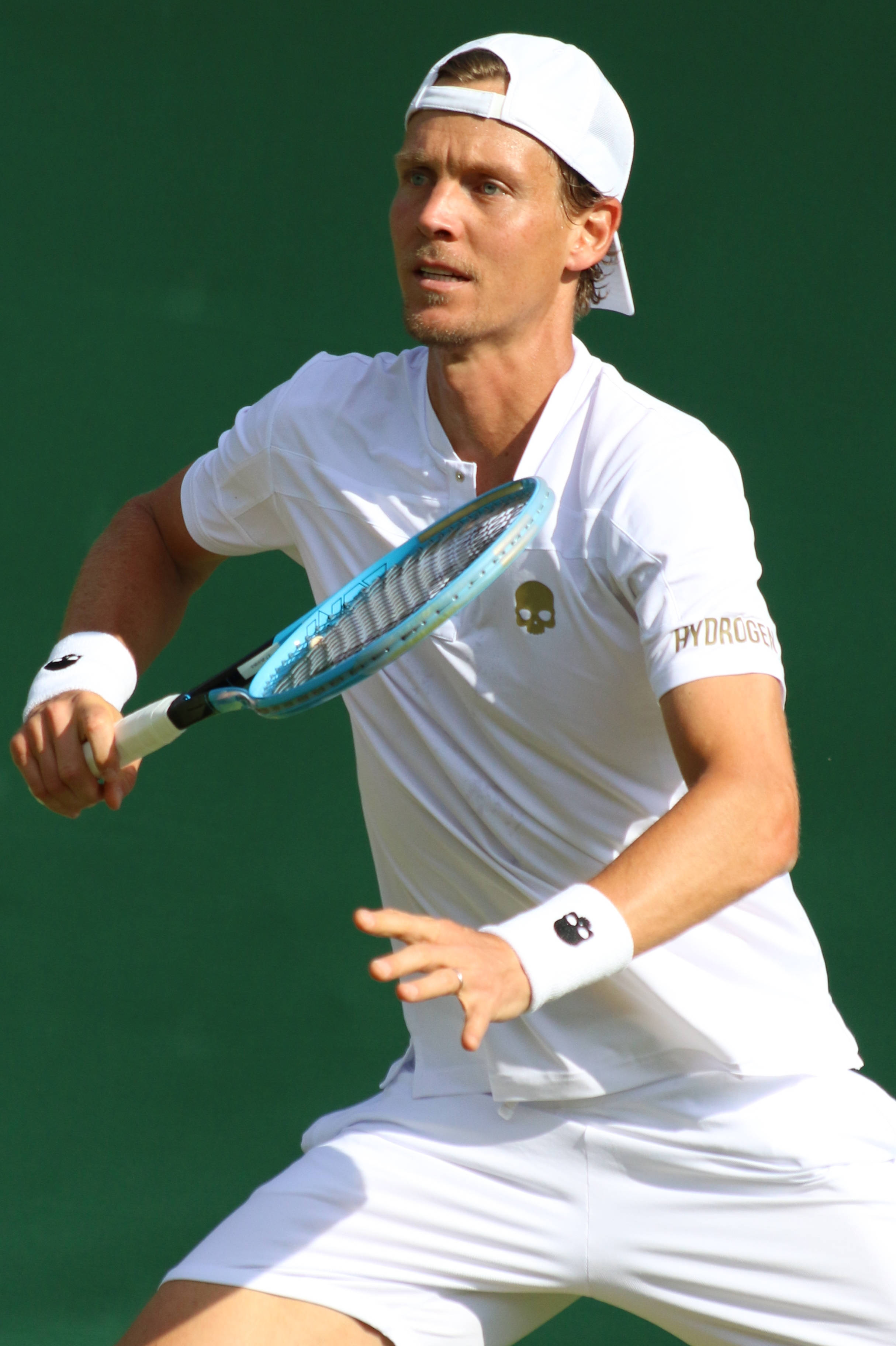Athlete 桌布 壁紙 — 一名身穿白色裝備的男性網球選手在純綠色球場背景下揮動藍色球拍。
