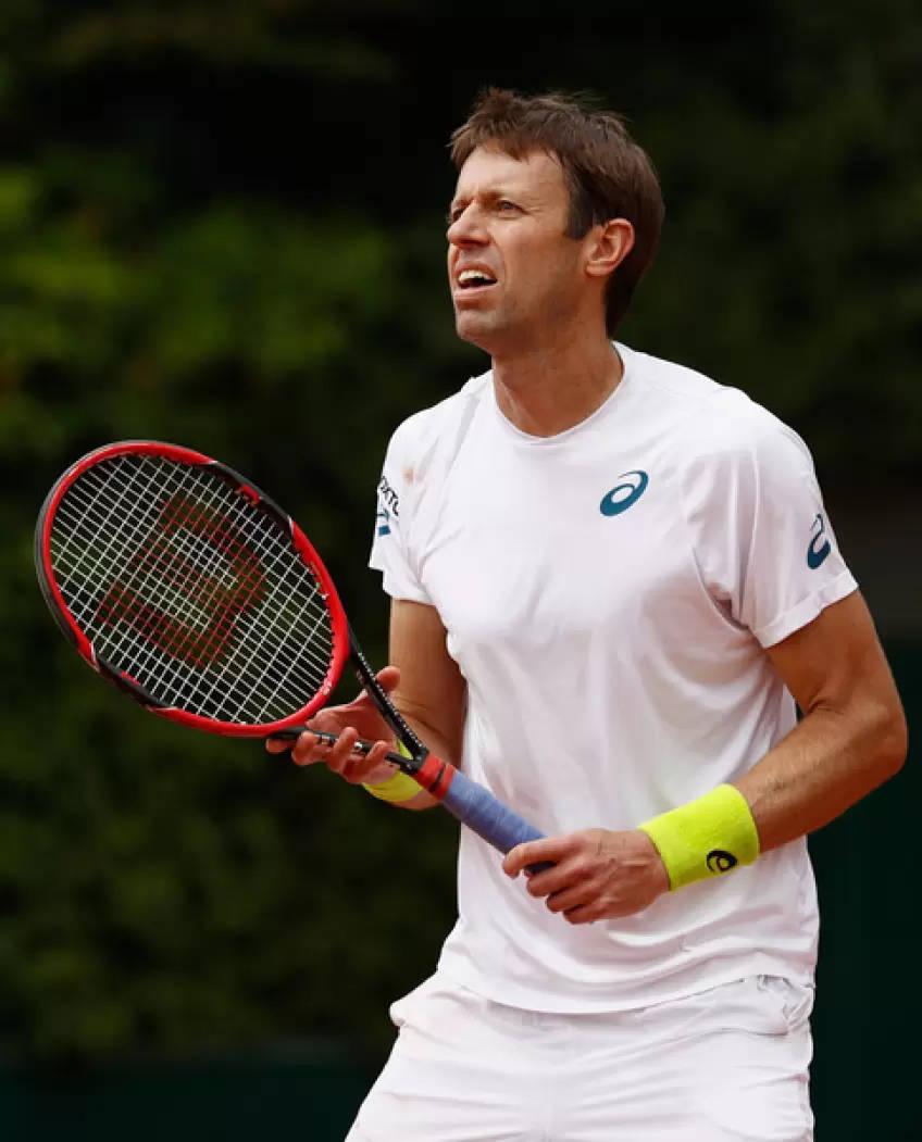 Tennis 桌布 壁紙 — 一名身穿白色裝備的男網球選手在比賽中，在模糊的綠色背景下，以強烈的專注力握著他的紅色球拍。