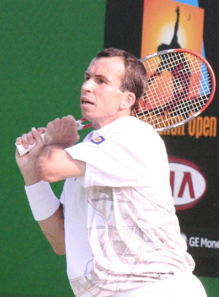 Tennis 桌布 壁紙 — 一名身穿白色裝備的男網球選手在綠色球場上比賽時，專注地揮動球拍。