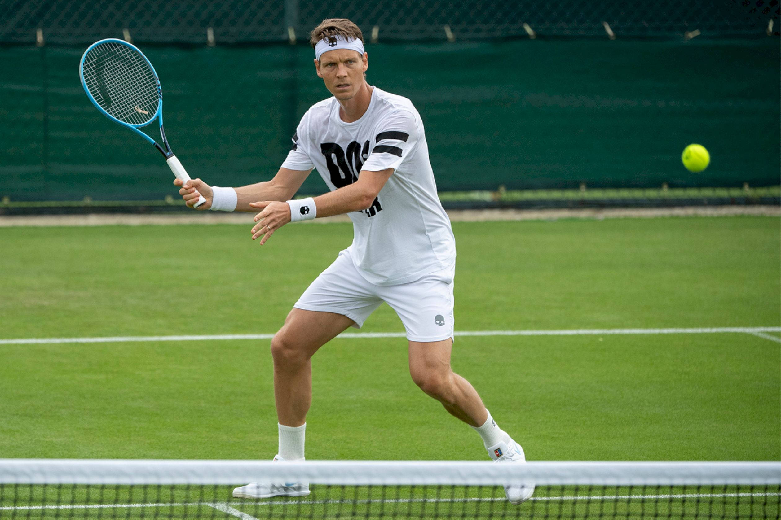 Tennis 桌布 壁紙 — 一名身穿白色裝備的男網球選手在草地場上向前撲出，用藍色球拍擊打一個亮黃色的球。