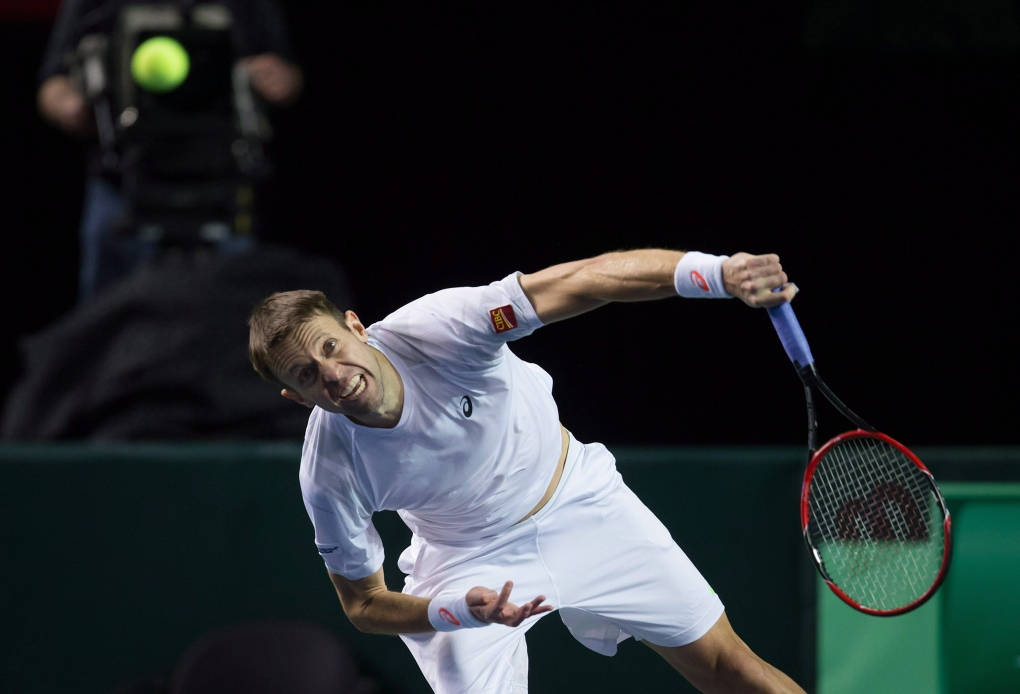 Tennis 桌布 壁紙 — 一名身穿白色裝備的男網球選手在體育館燈光下，以強烈的專注力向前猛衝，擊打一個亮黃色的球。