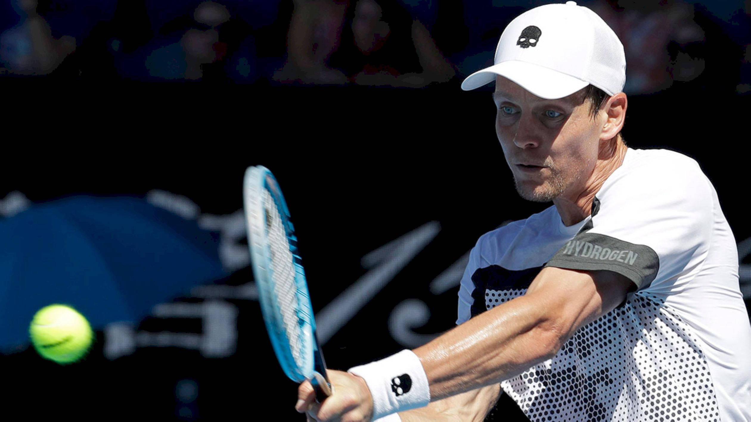 Tennis 桌布 壁紙 — 一名身穿白色裝備的男網球選手在體育館燈光下揮動藍色球拍擊打亮黃色網球。