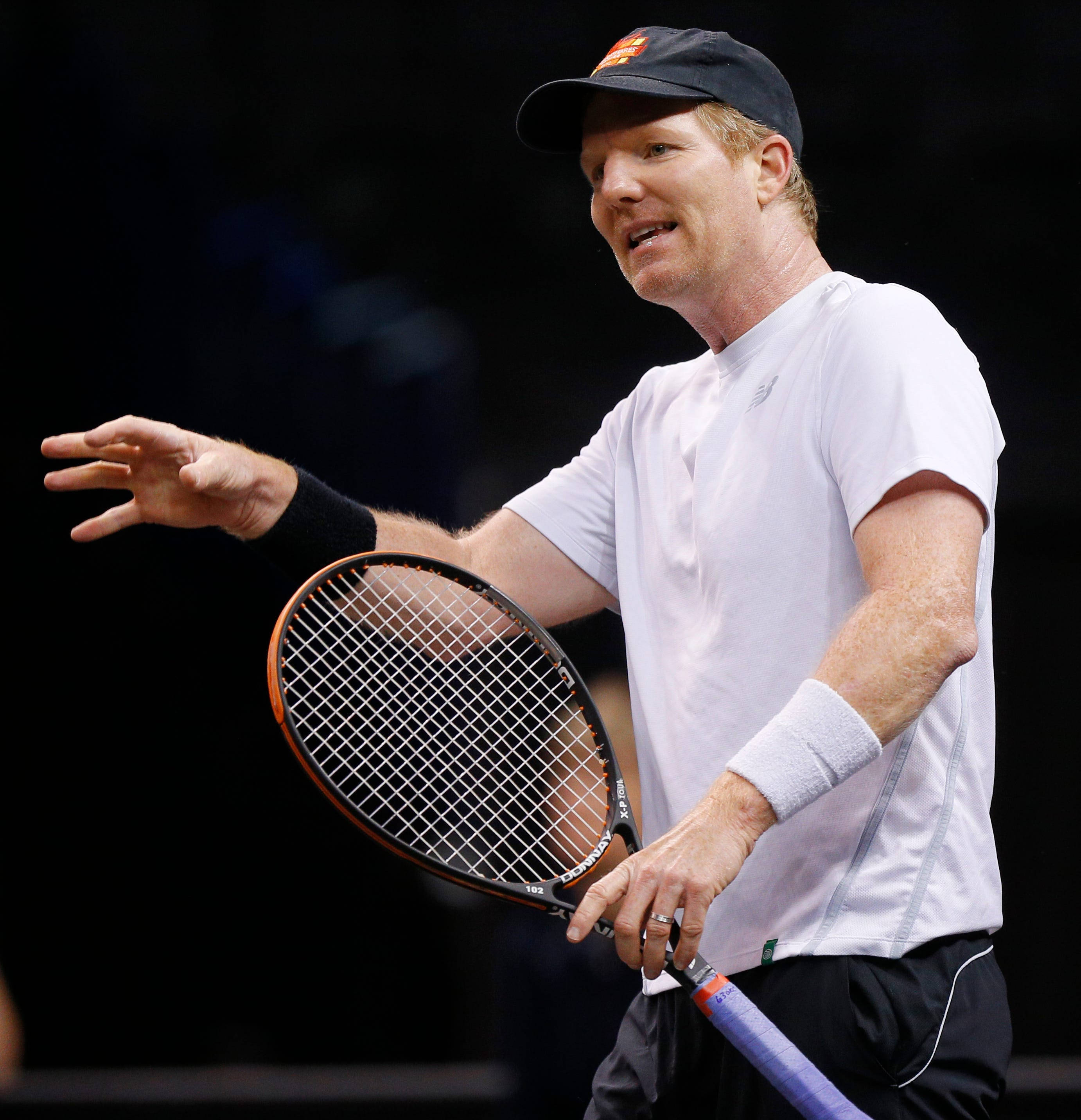 Tennis 桌布 壁紙 — 一名身穿白色襯衫和帽子的男性網球運動員在深色背景下拿著球拍生動地做手勢。