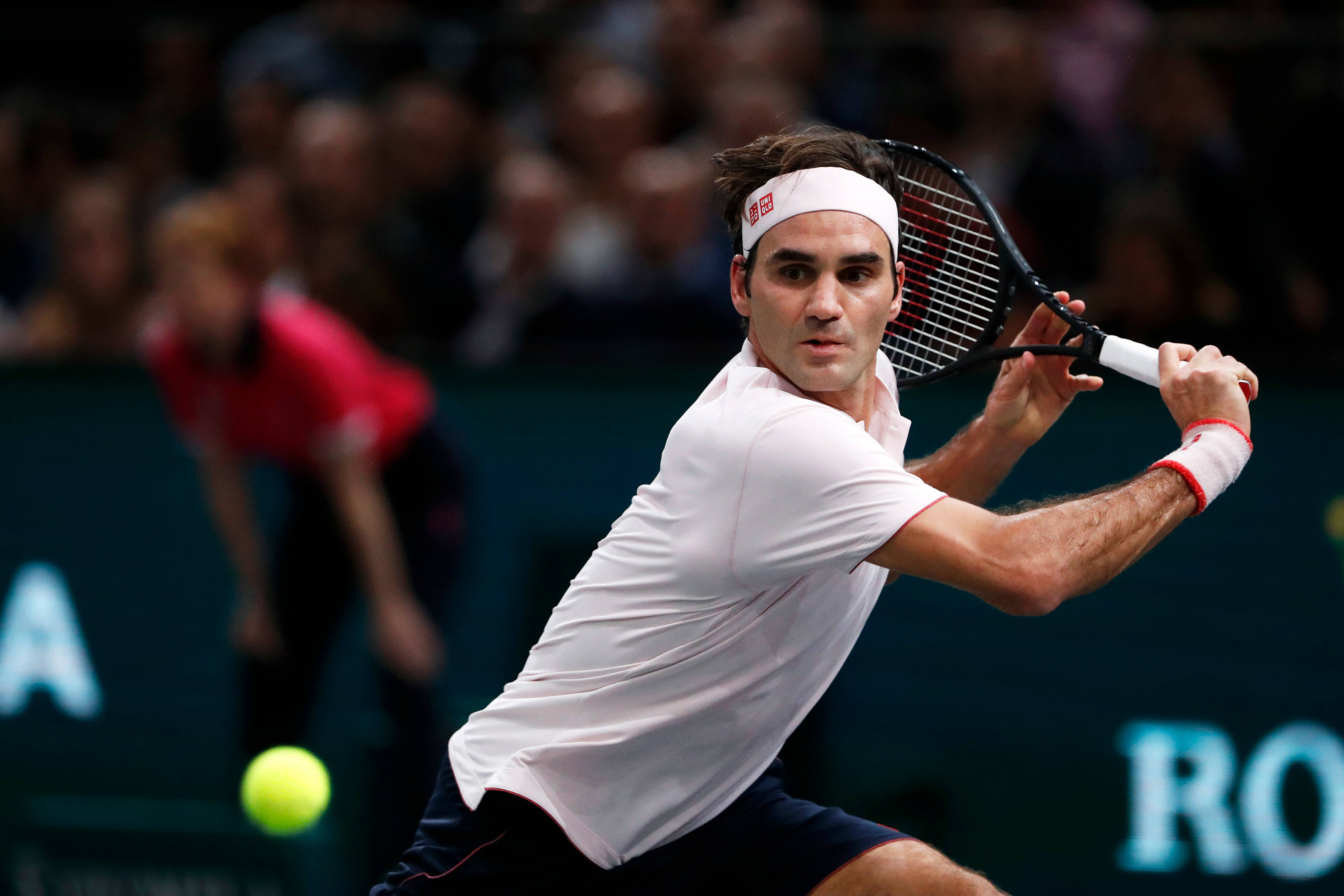 roger 桌布 壁紙 — 一名身穿白色襯衫和頭帶的男性網球選手在比賽中揮拍擊打黃色球，背景有模糊的觀眾。