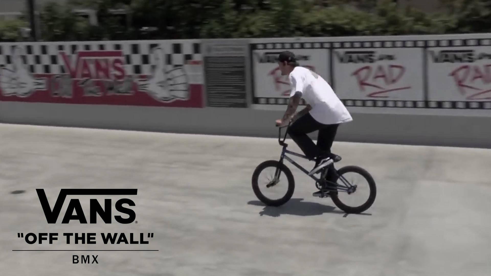 Vans Off The Wall 桌布 壁紙 — 一名身穿白色襯衫和黑色褲子的BMX車手在混凝土坡道上表演技巧，背景是Vans塗鴉牆。