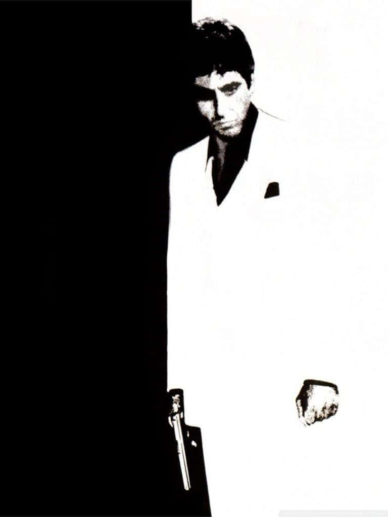 Al Pacino 桌布 壁紙 — 一名身穿白色西裝的男子，在強烈的黑白對比中站立，手持槍支，表情嚴肅。