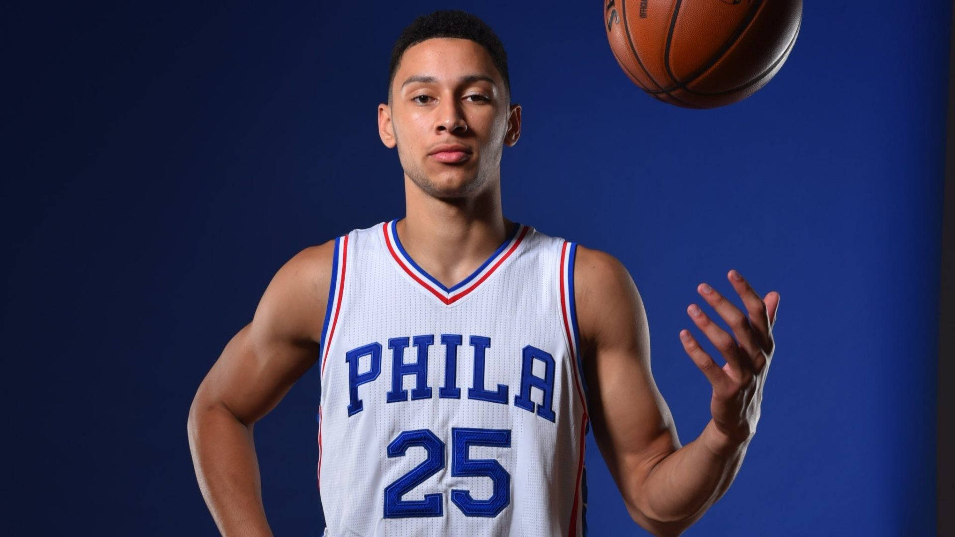 Ben Simmons 桌布 壁紙 — 一名身穿白色費城球衣、號碼25的籃球運動員在純藍色攝影棚背景前，將球平衡在半空中。
