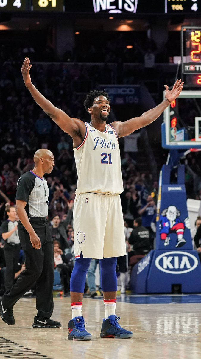 NBA 桌布 壁紙 — 一名身穿白色費城球衣的籃球運動員在燈光明亮的球場上比賽時高舉雙臂慶祝勝利。