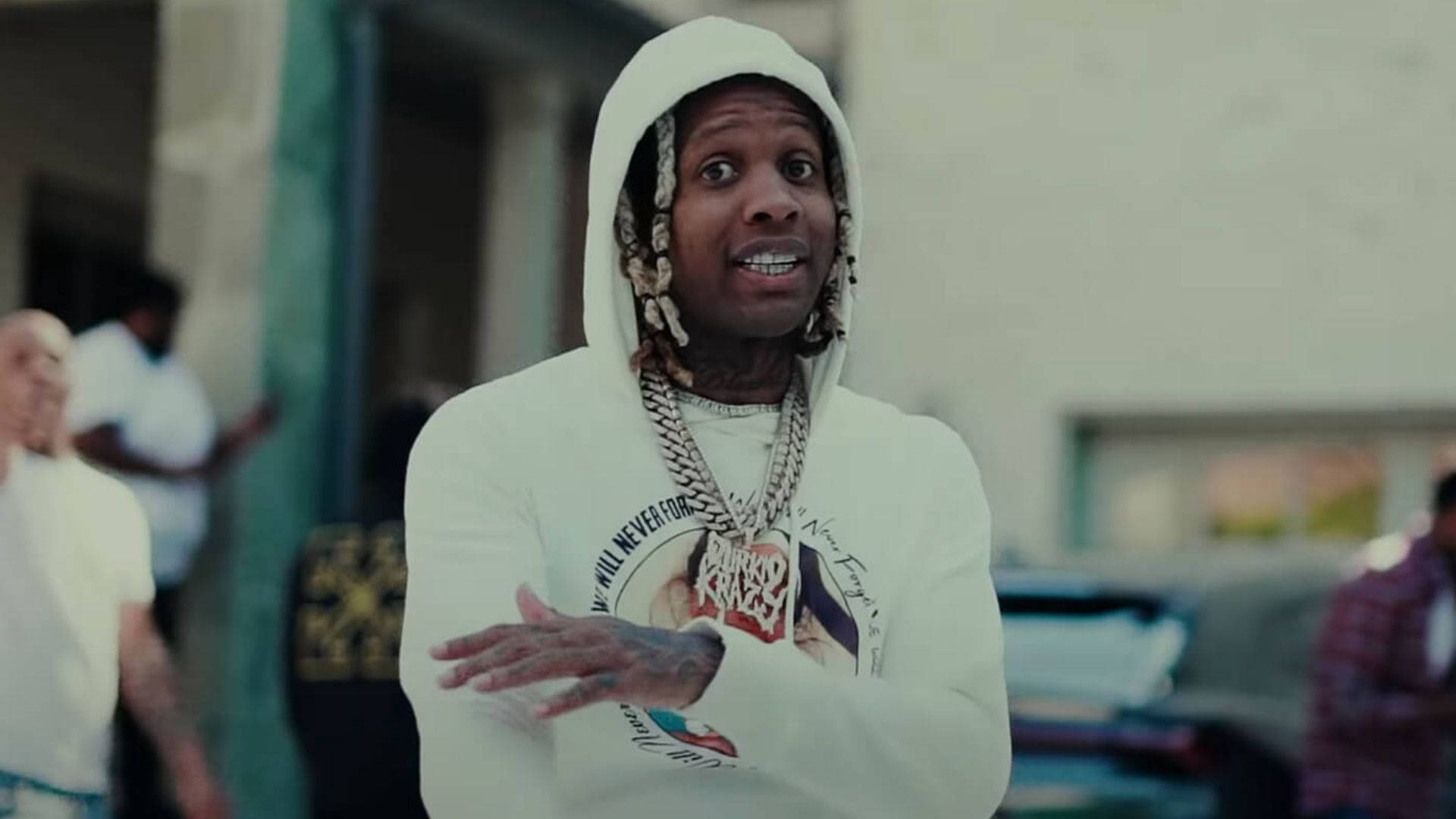 Lil Durk 桌布 壁紙 — 一名身穿白色連帽衫、辮子頭髮和粗鏈條的男子在戶外生動地做手勢。
