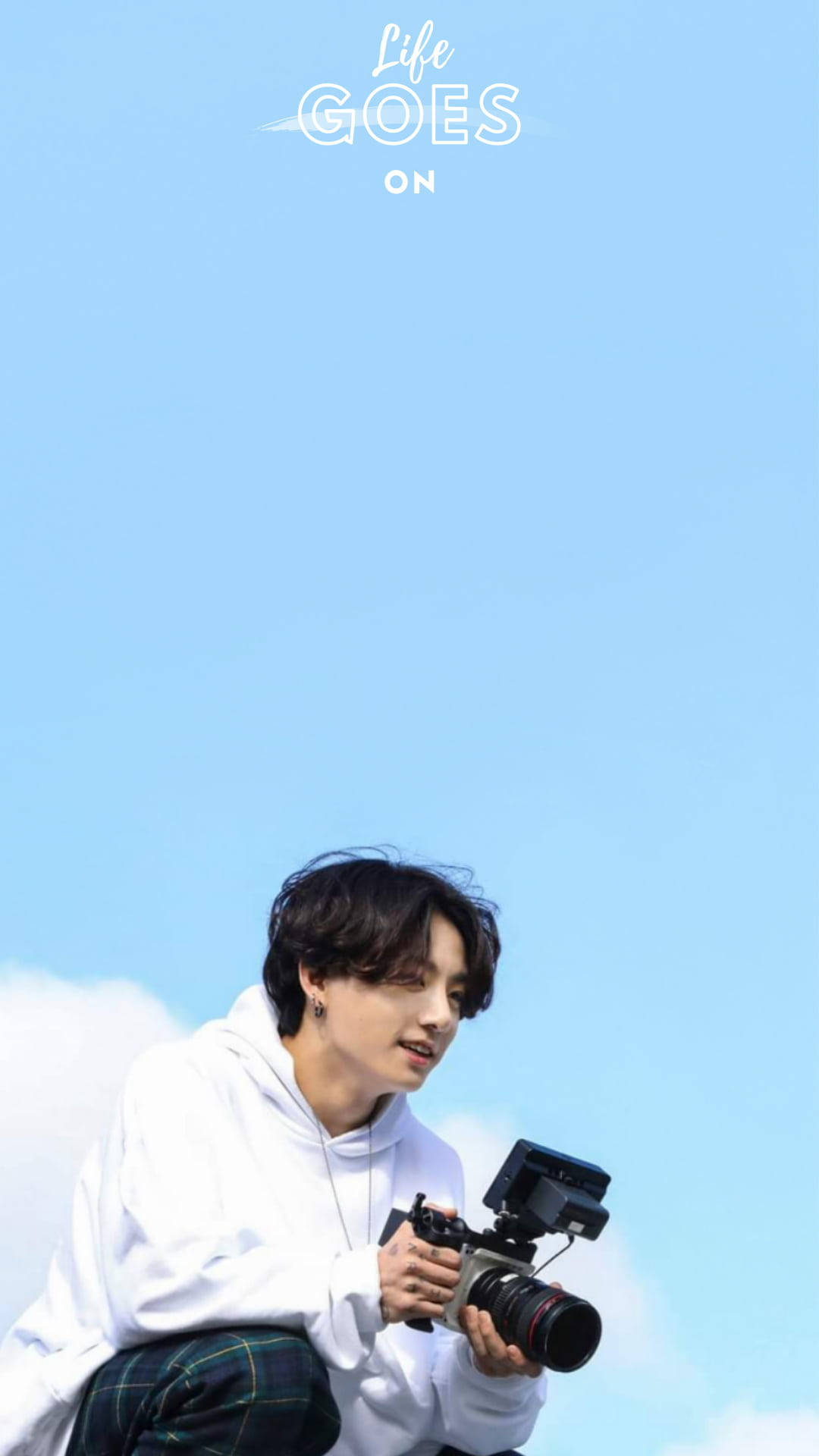 BTS 桌布 壁紙 — 一名身穿白色連帽衫的年輕男子，在晴朗的藍天白雲下拿著相機。