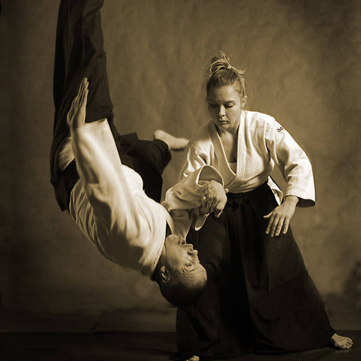 martial arts 桌布 壁紙 — 一名身穿白色道服的女人，在柔和的攝影棚背景下，對一個身穿黑色道服的男人執行一個動態的投擲動作。