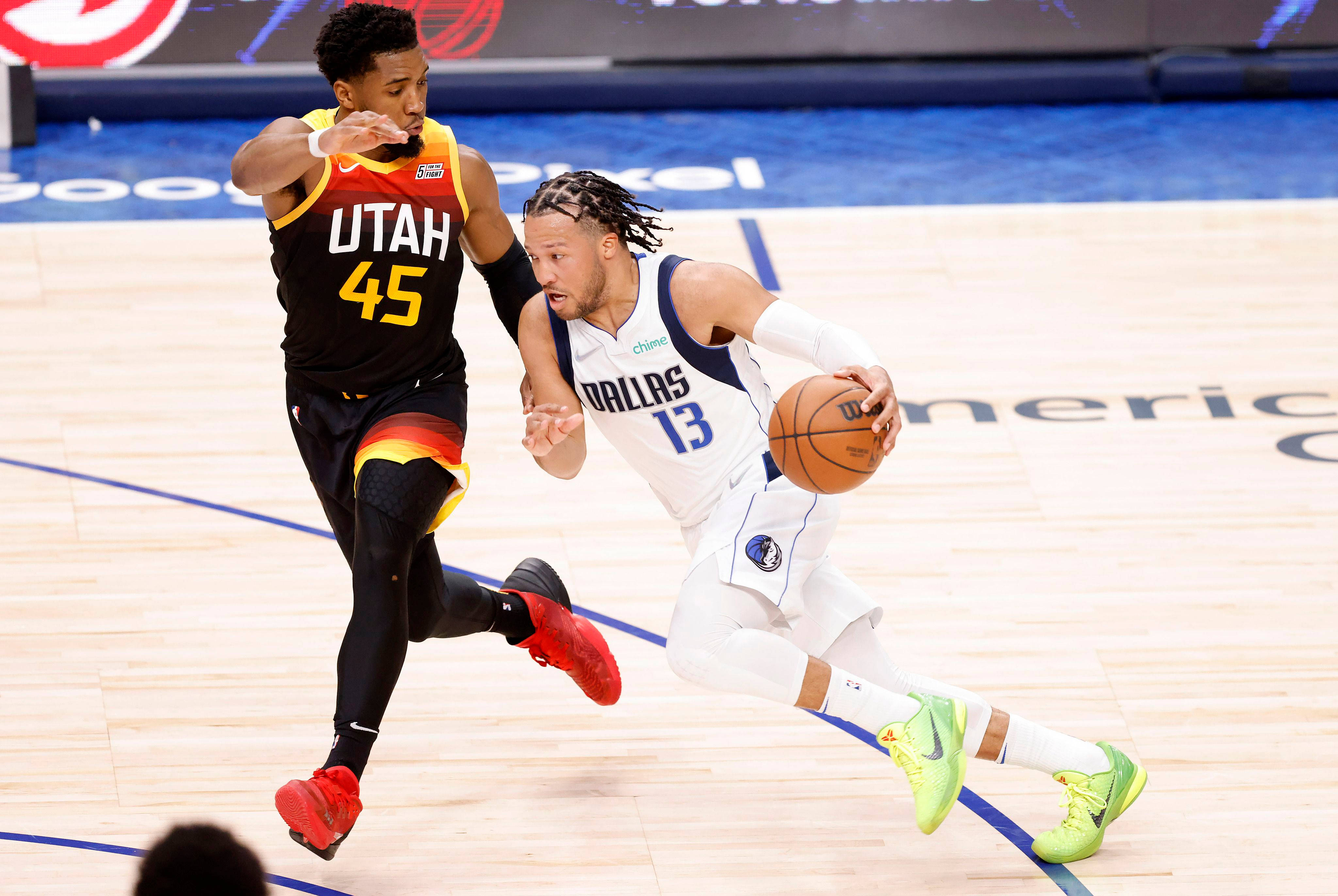 NBA 桌布 壁紙 — 一名身穿白色達拉斯球衣的籃球運動員在燈光明亮的球場上運球，同時被一名身穿黑色猶他球衣的對手緊密防守。