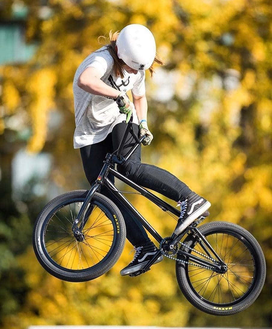 腳踏車 桌布 壁紙 — 一名身穿白色頭盔和灰色襯衫的BMX車手，在金色秋樹的背景下，騎著黑色自行車騰空而起。