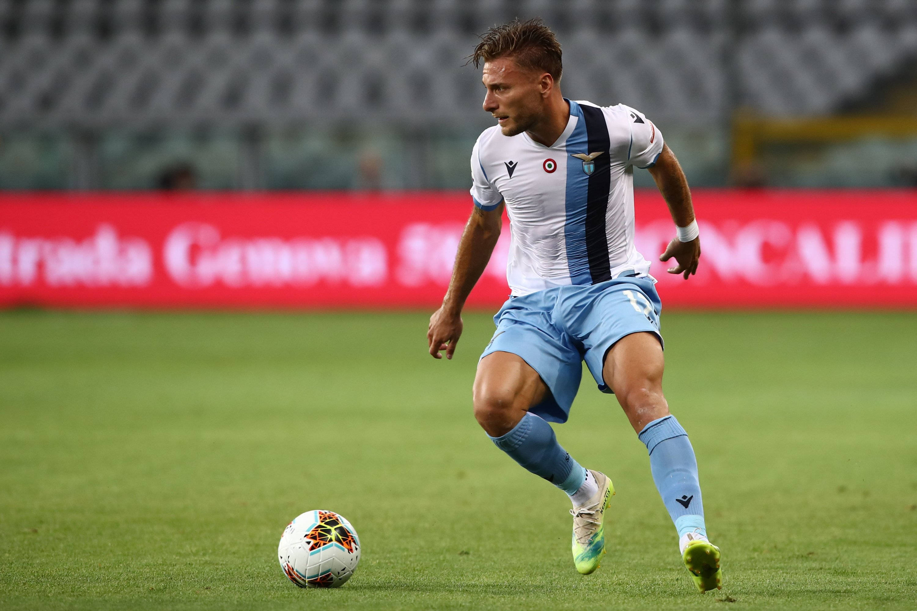 ciro immobile 桌布 壁紙 — 一名身穿白藍間條球衣的足球運動員在體育場燈光下，於充滿活力的綠色球場上運球。