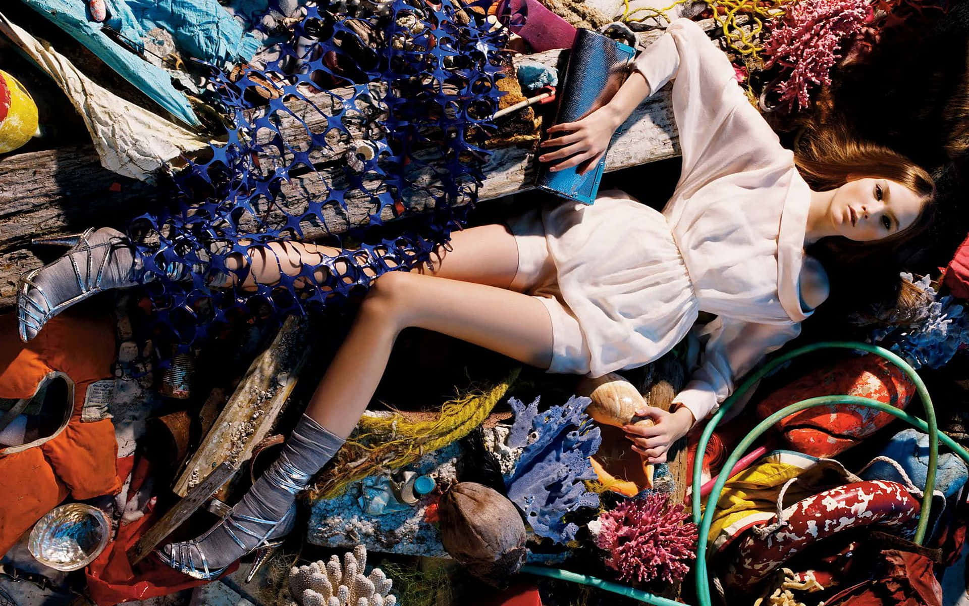 Spring Fashion 桌布 壁紙 — 一名身穿白衣的女子在明亮的陽光下，躺在一堆色彩繽紛的海洋垃圾和珊瑚上。